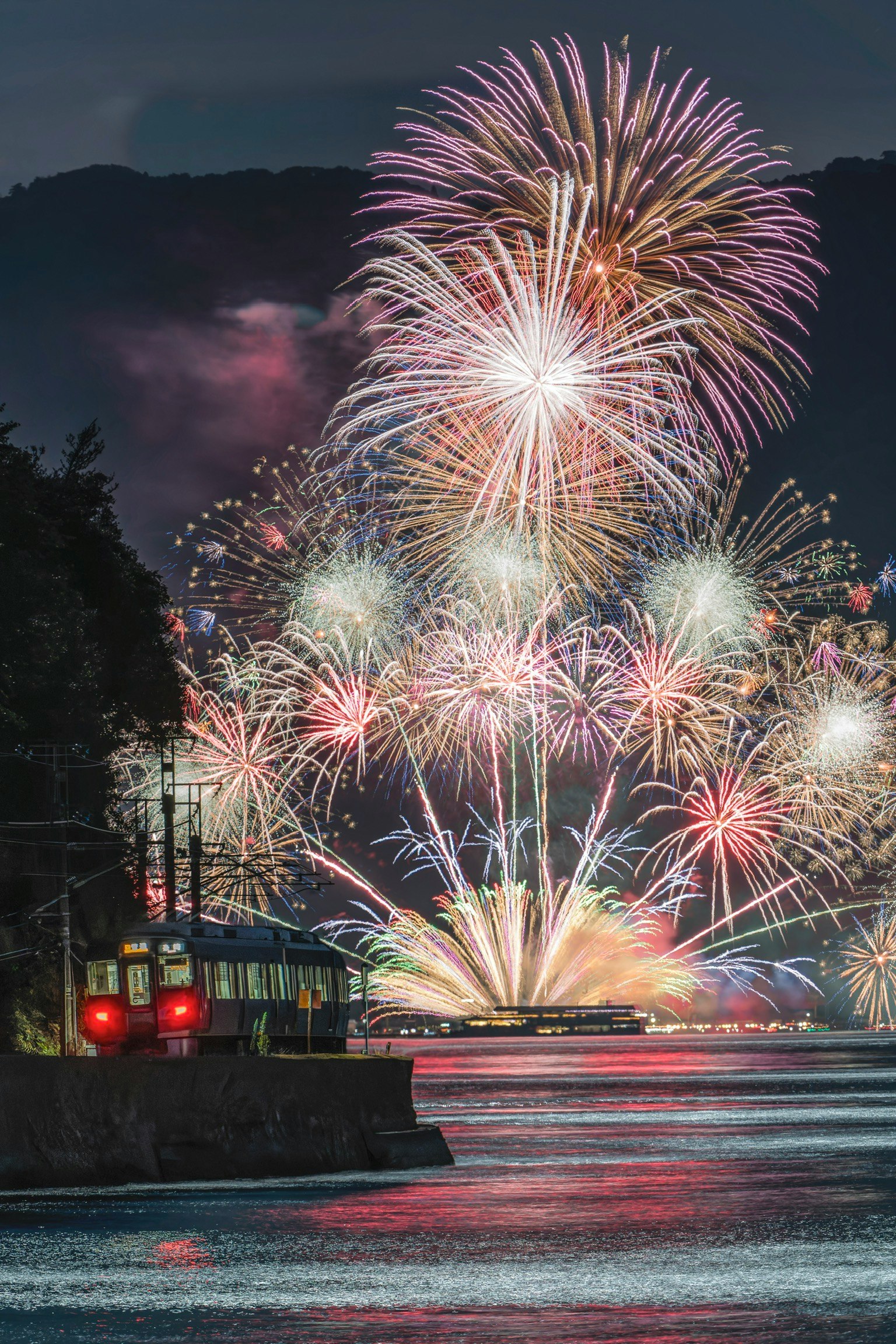 瀬戸田夏まつり2025の花火と呉線の電車が夜の海上を通過する様子