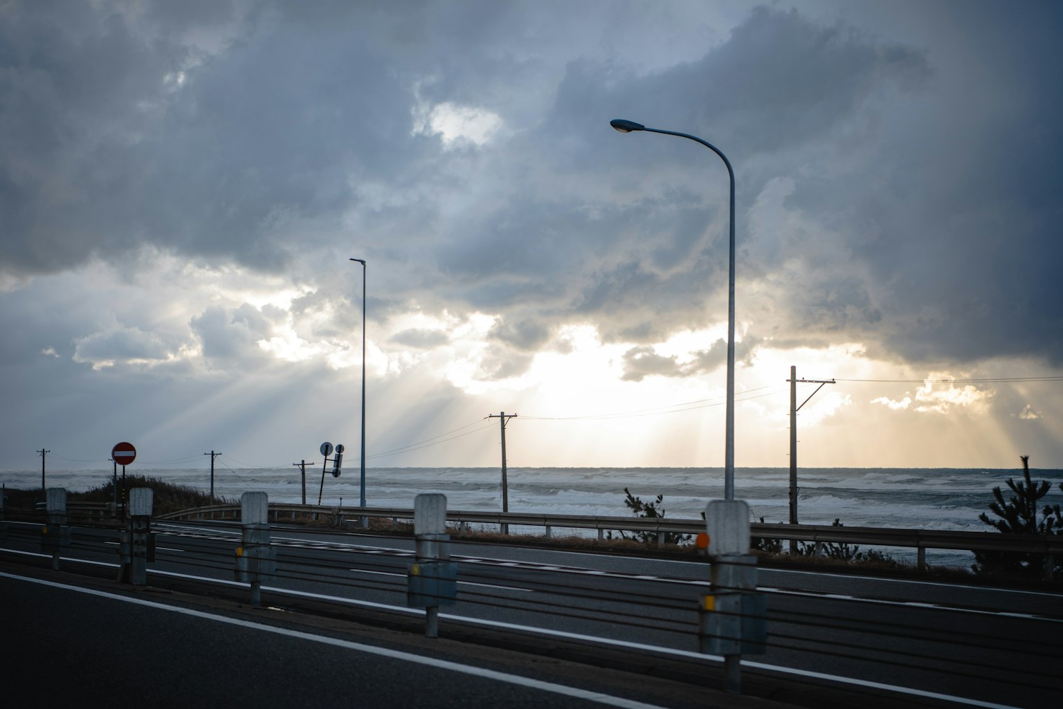 Vista di una strada costiera con nuvole scure e raggi di luce che filtrano