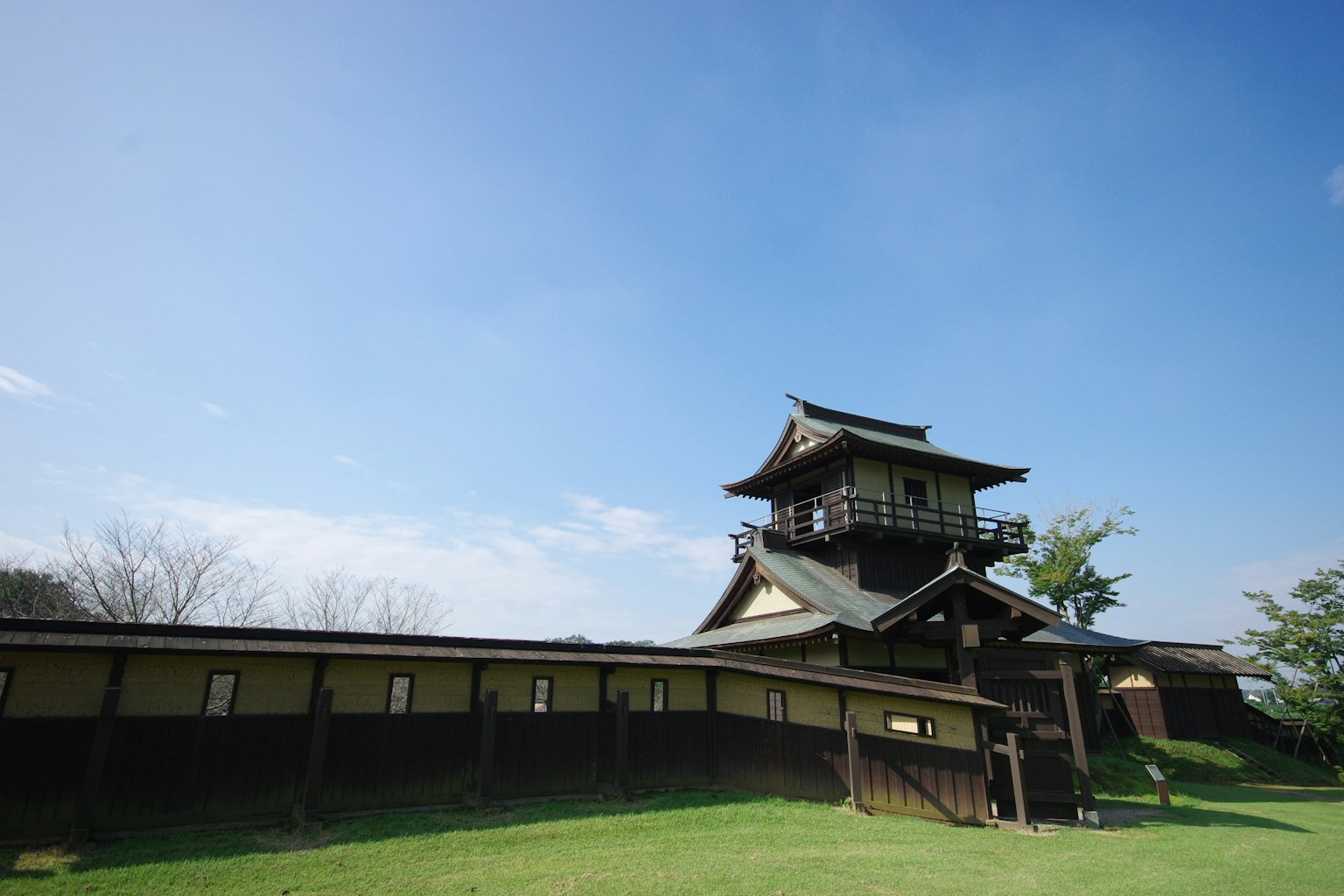 Japanese castle structure under a blue sky with green grass