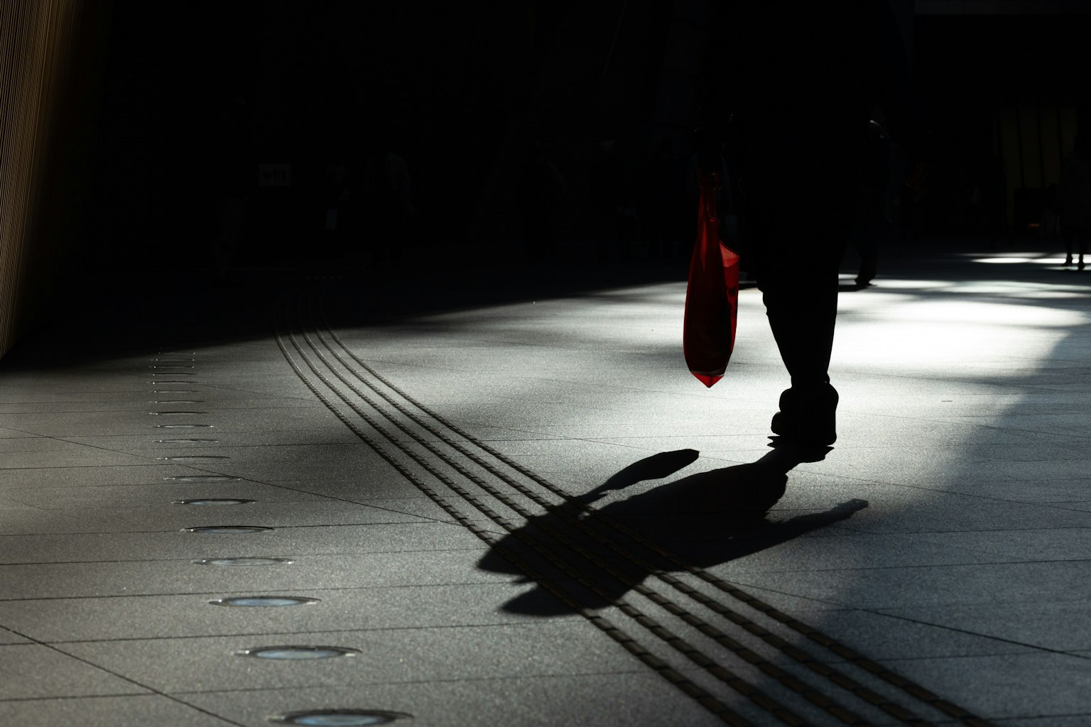 Silueta de una persona caminando con un paraguas rojo proyectando una sombra en el suelo