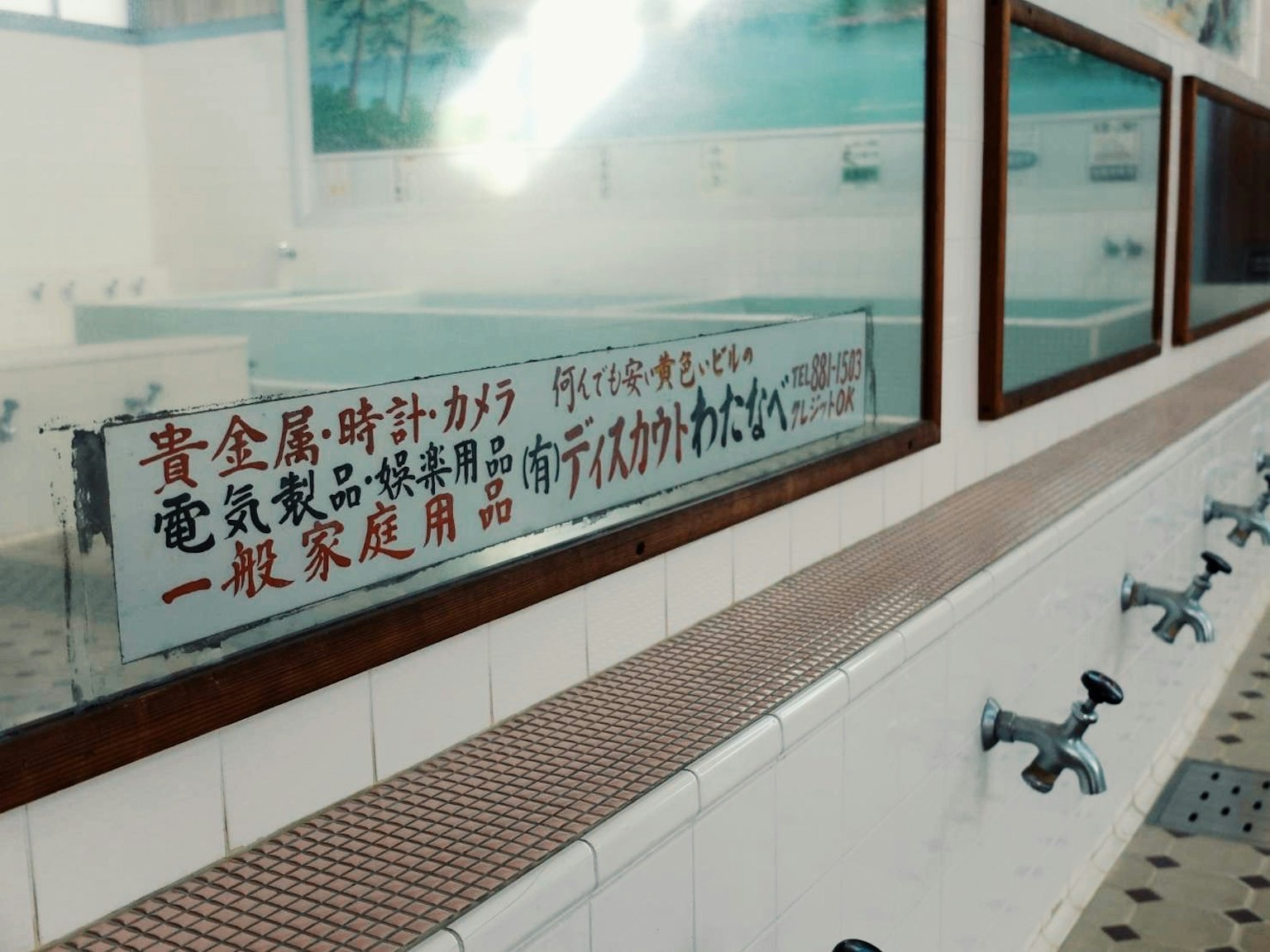 Vue intérieure d'une salle de bain avec des lavabos et des miroirs affichant un avis en japonais sur le mur