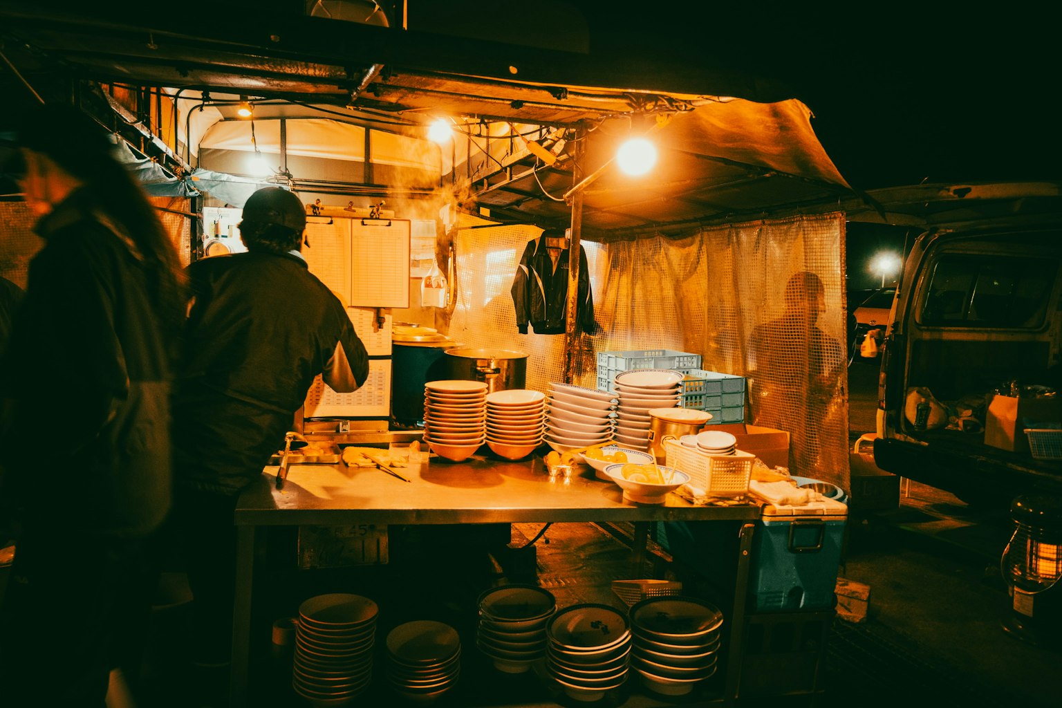 夜市攤位，有人正在烹飪，桌上堆放著盤子