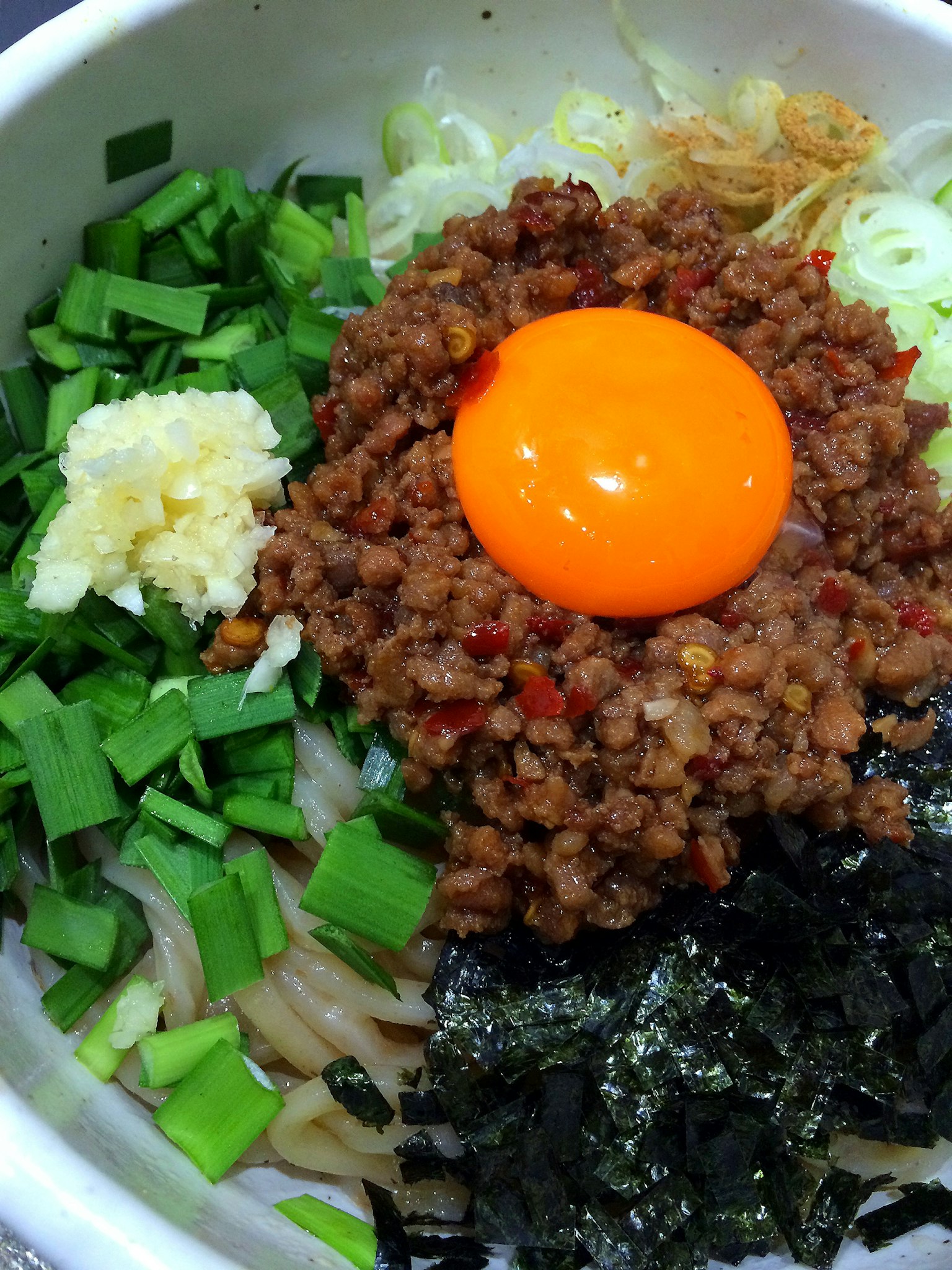 Ciotola di noodle guarnita con carne macinata e tuorlo d'uovo crudo circondato da cipollotti e alga