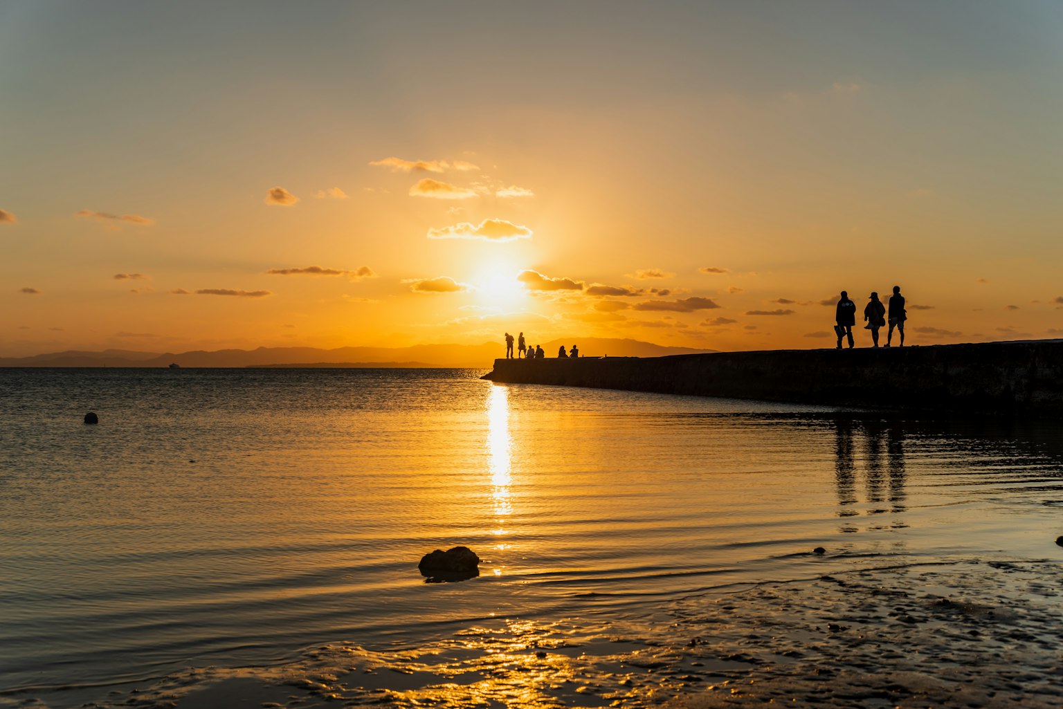 Silhouettes of people walking along the coastline at sunset