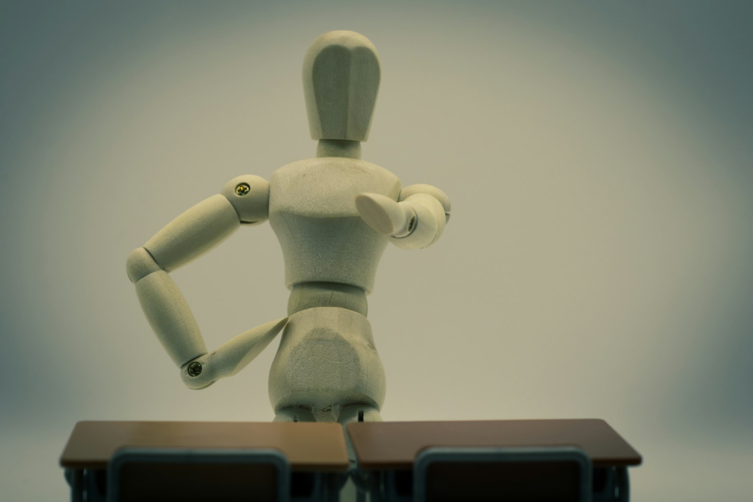 A wooden mannequin standing at a desk gesturing