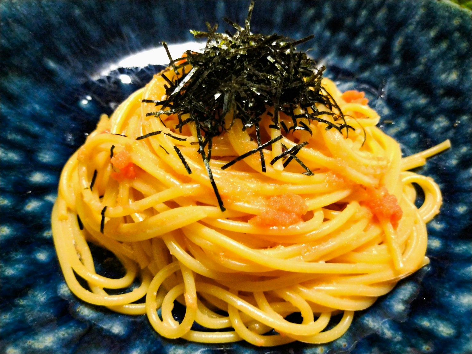 Spaghetti topped with seaweed served on a blue plate