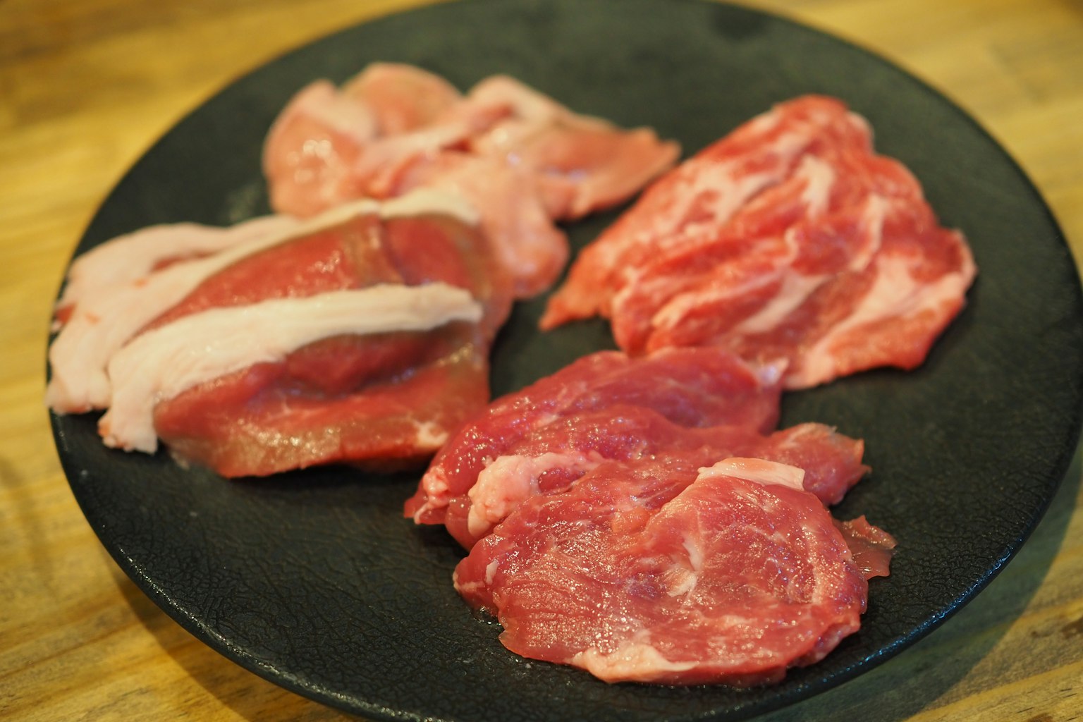 Verschiedene Arten von rohem Fleisch auf einem schwarzen Teller angeordnet