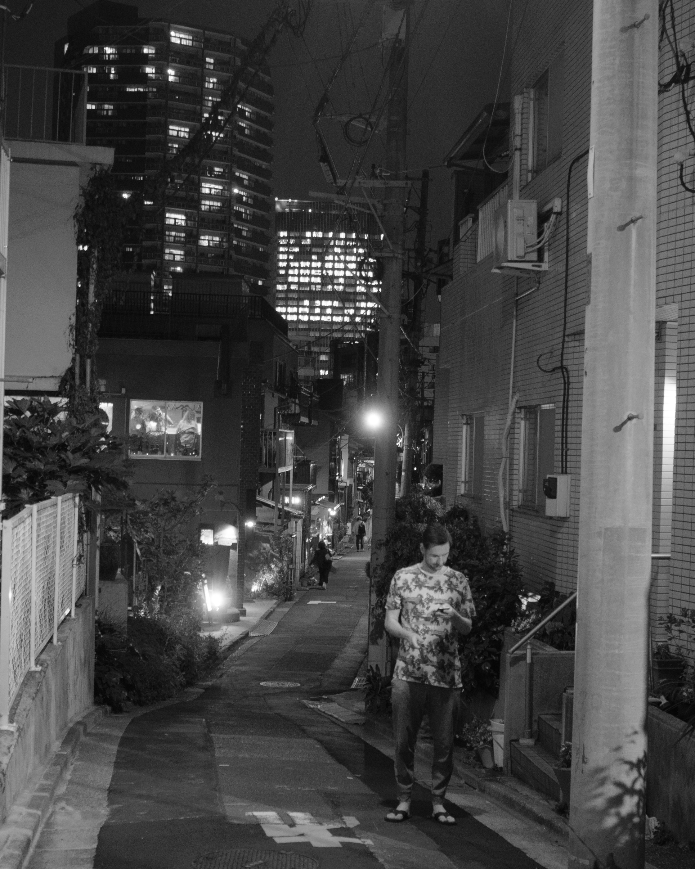 高層ビルに挟まれた路地を歩く人物のある夜景