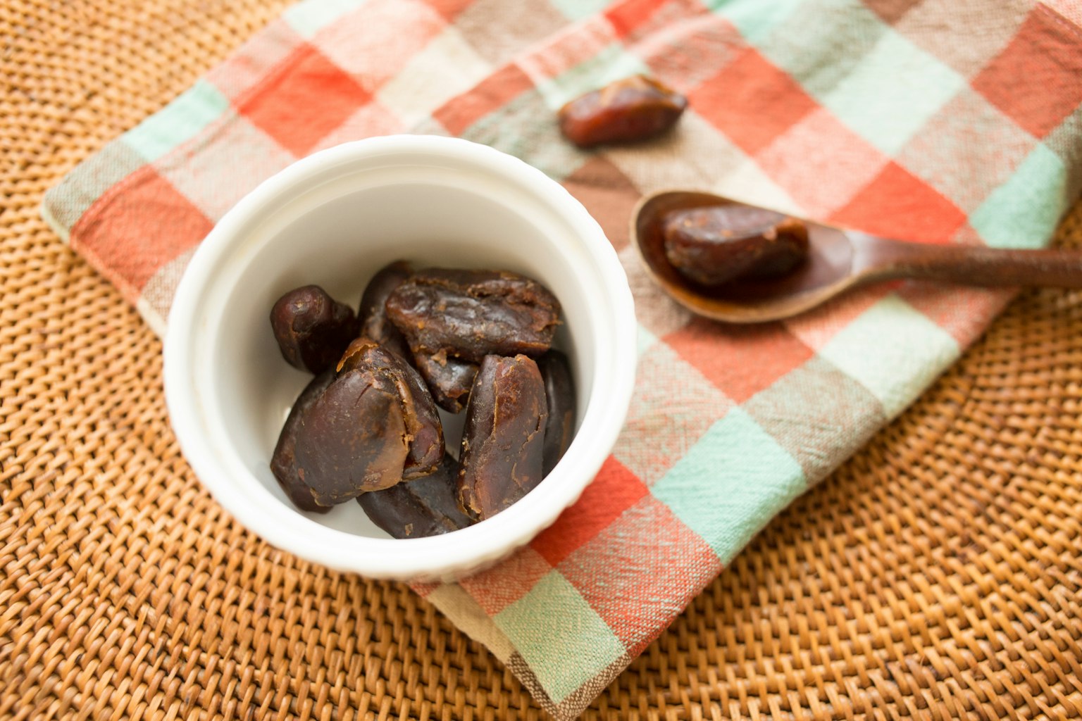 A white bowl filled with dates on a checkered napkin