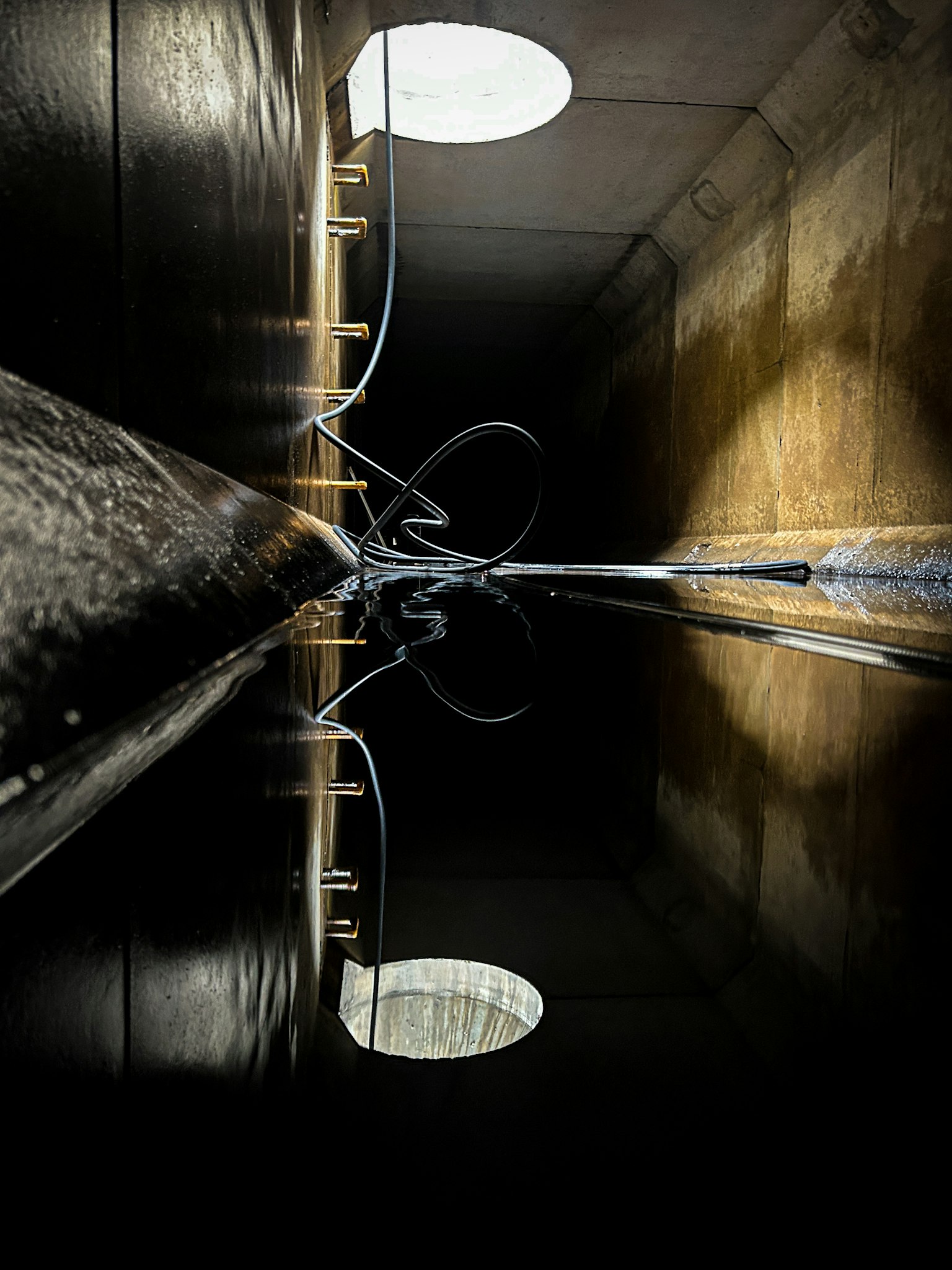 Inneres eines dunklen Tunnels mit reflektierender Wasseroberfläche Lichter, die sich an den Wänden spiegeln