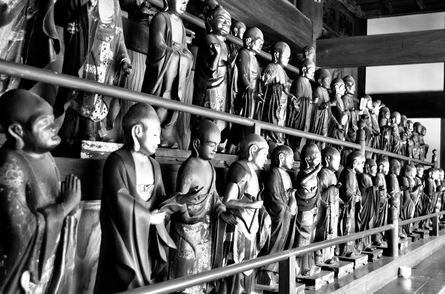 Schwarzweißfoto von zahlreichen Buddha-Statuen, die in einem Tempel aufgereiht sind