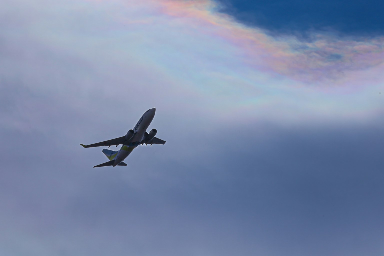 An airplane flying against a blue sky with colorful clouds