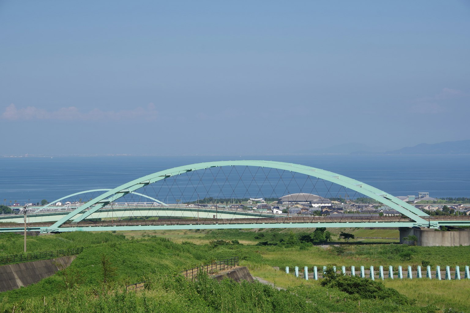 Jembatan lengkung hijau di latar belakang laut biru dan padang rumput hijau