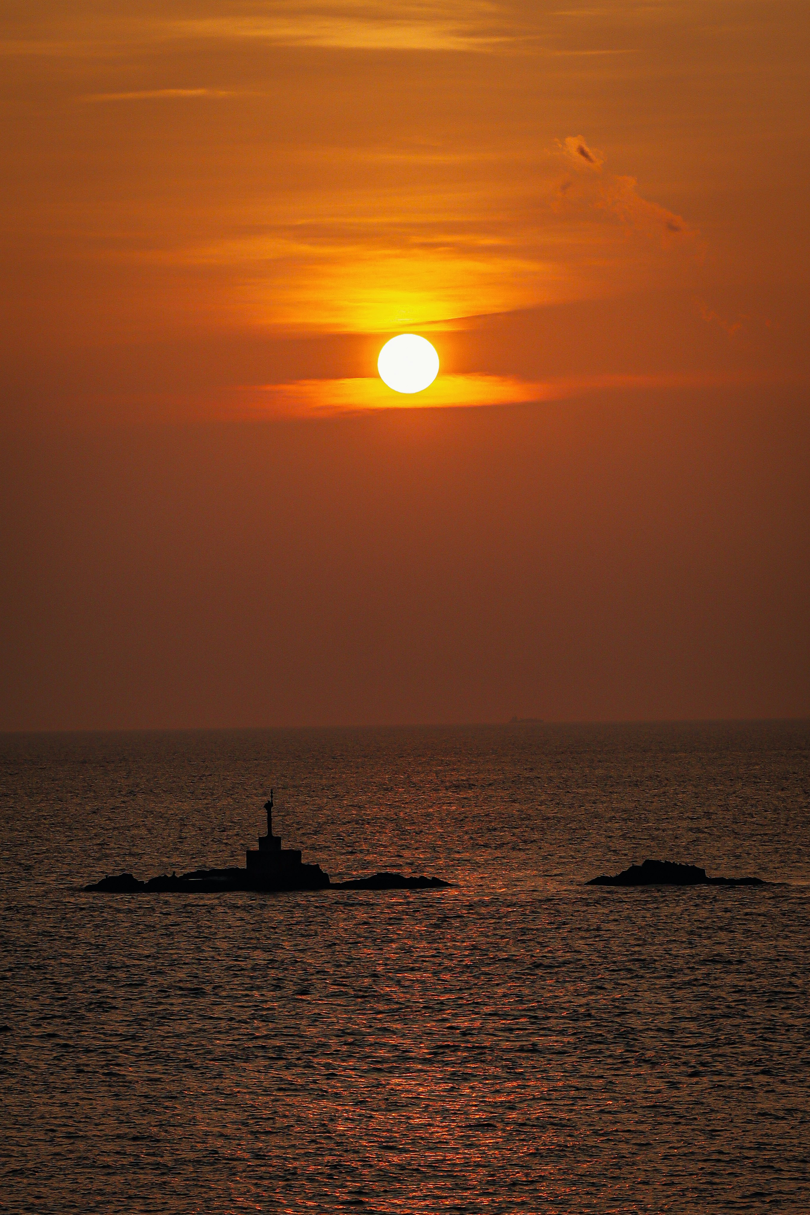 夕日に照らされる灯台と海の水平線