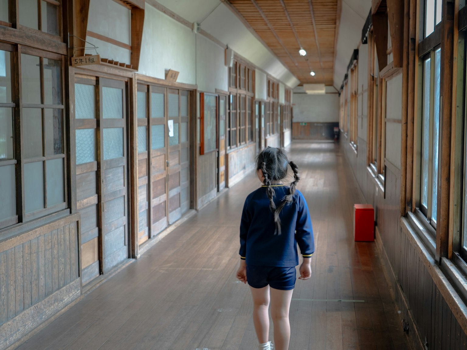 Una ragazza che cammina in un vecchio corridoio di scuola con pavimenti in legno e grandi finestre
