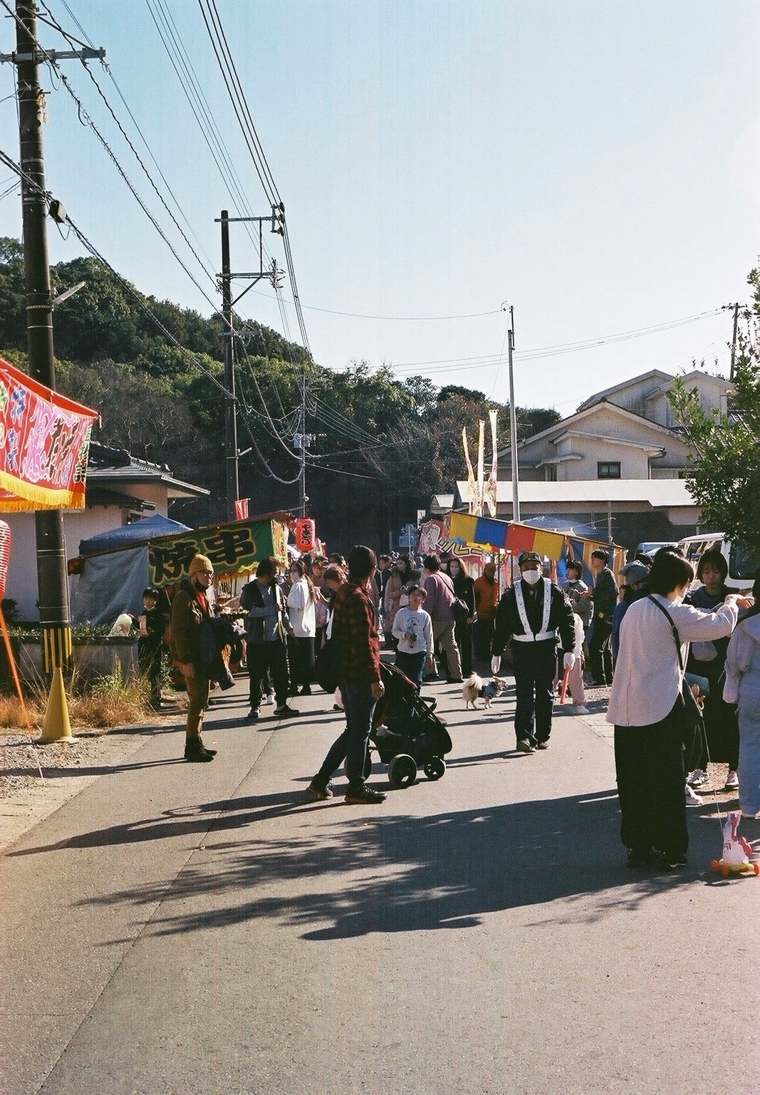 山あいの道で行列する人々と屋台の旗が並ぶ祭りの通り