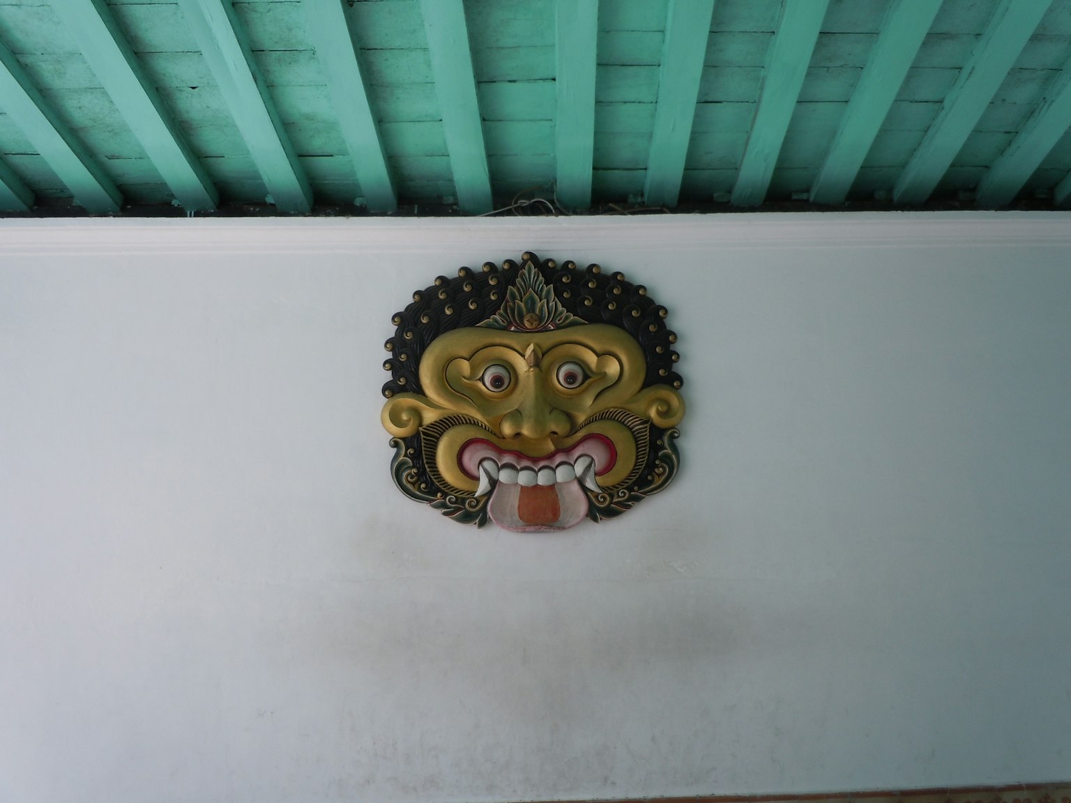 Scultura di maschera balinese tradizionale sotto un soffitto blu