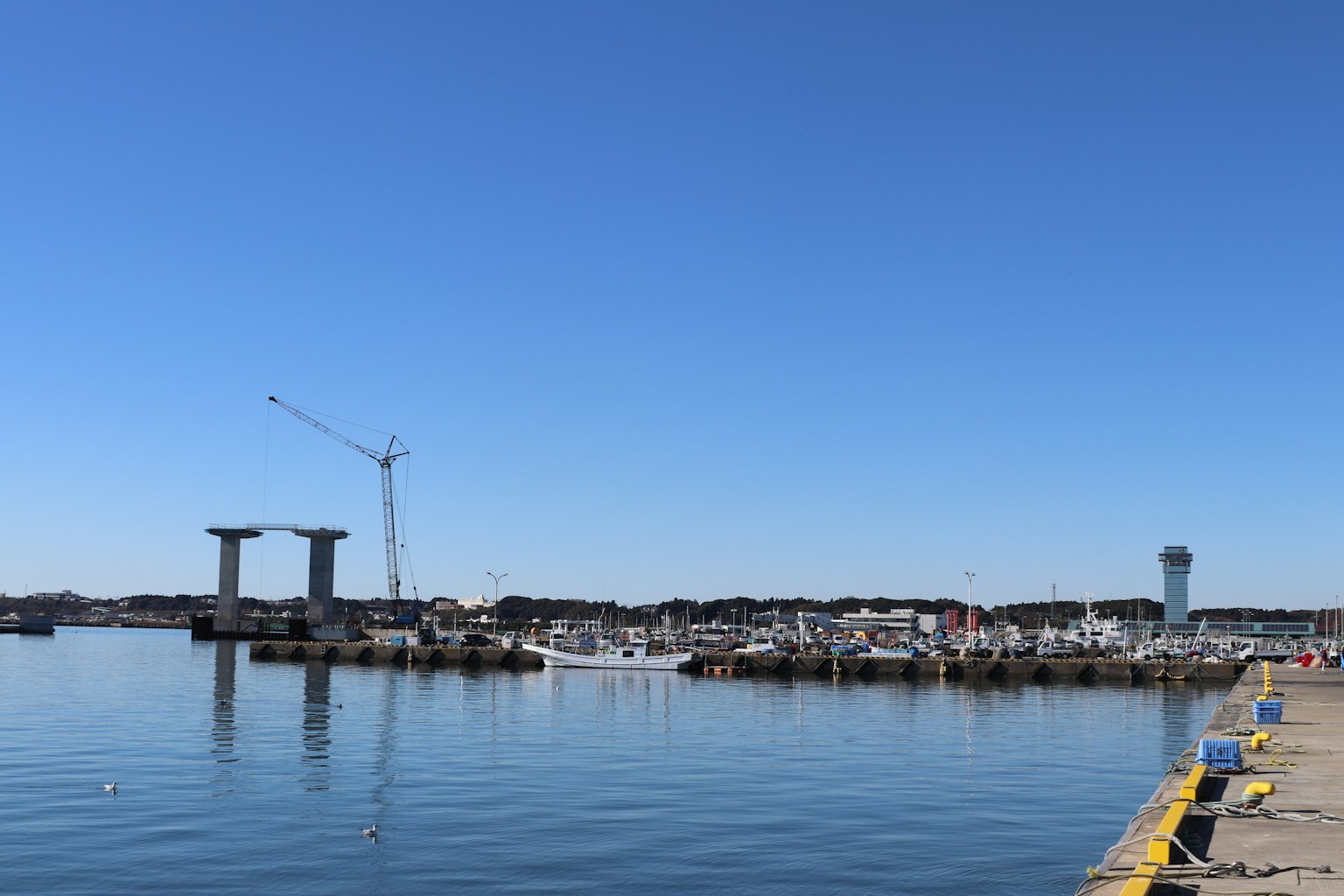 Harbor view under a clear blue sky featuring a crane and yachts