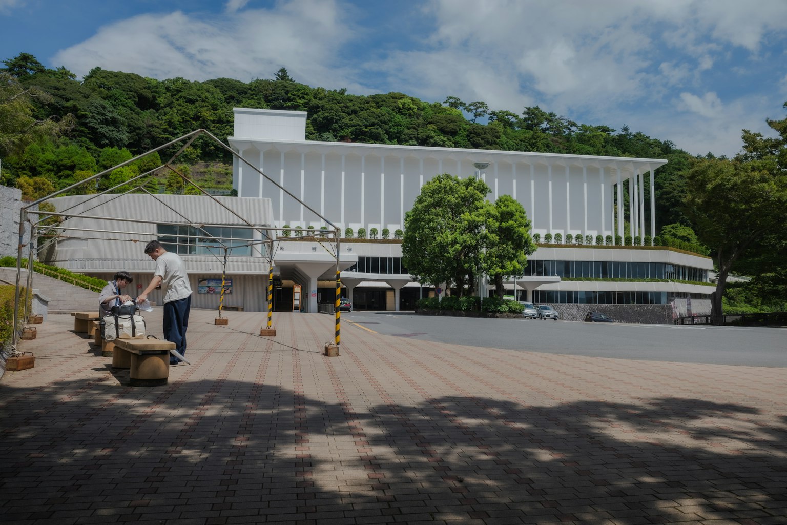白い建物と緑の木々がある風景で人が作業している