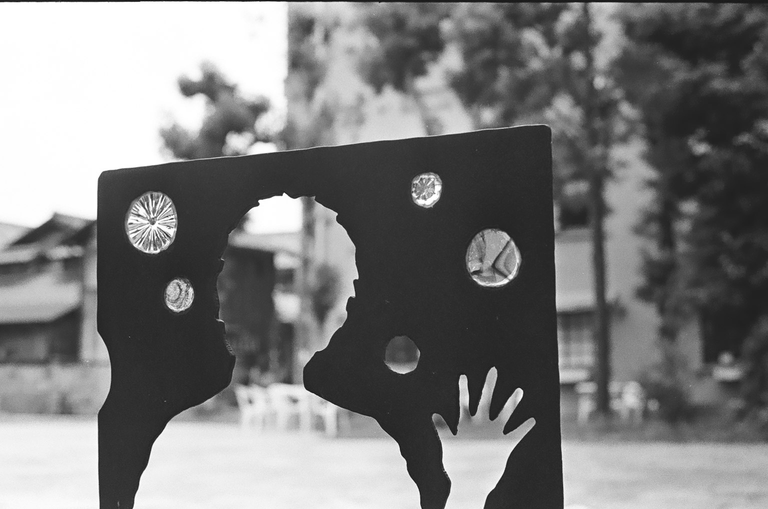 검은색 아트 작품에 컷아웃 디자인과 원형 구멍이 있으며 배경에는 나무와 건물이 보인다