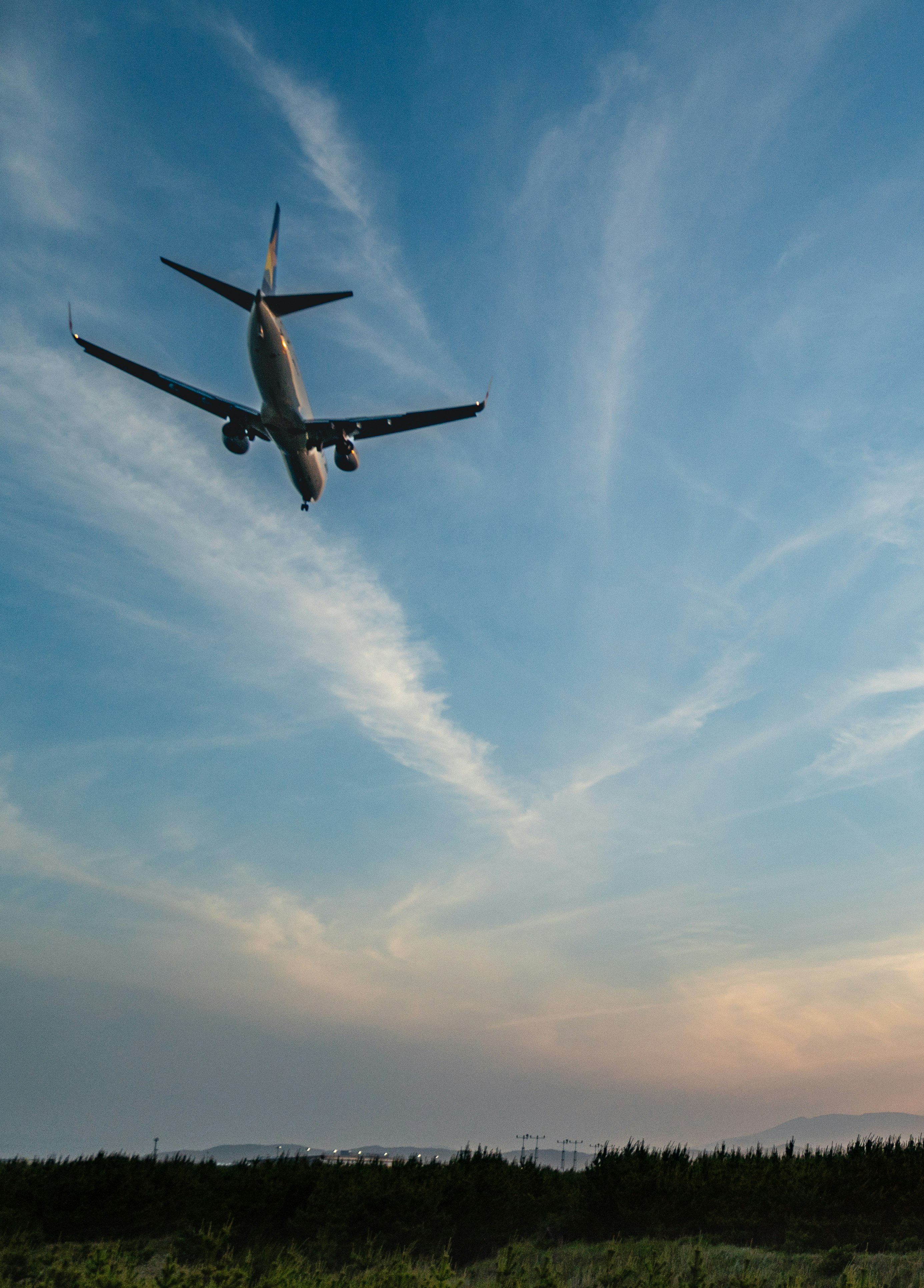 夕焼け空を飛ぶ飛行機と雲の流れ、海と山を望む景色