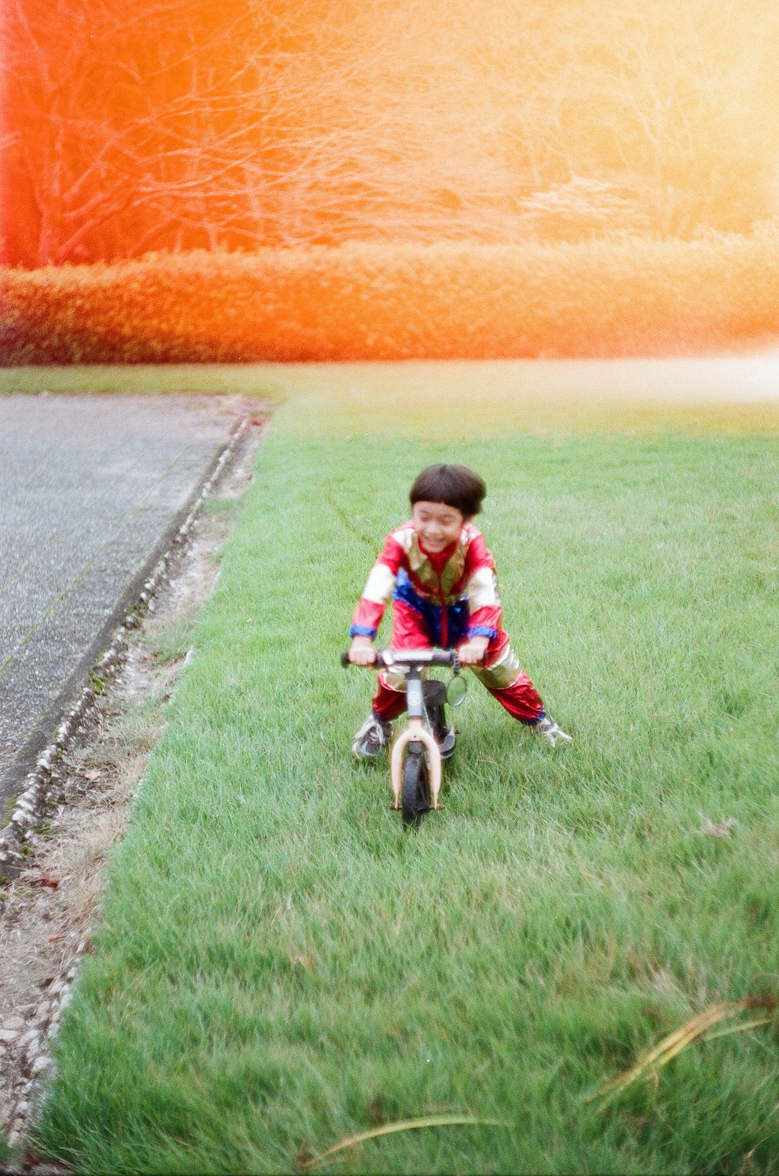 芝生の上でバランスバイクに乗る子供 明るいオレンジ色の背景