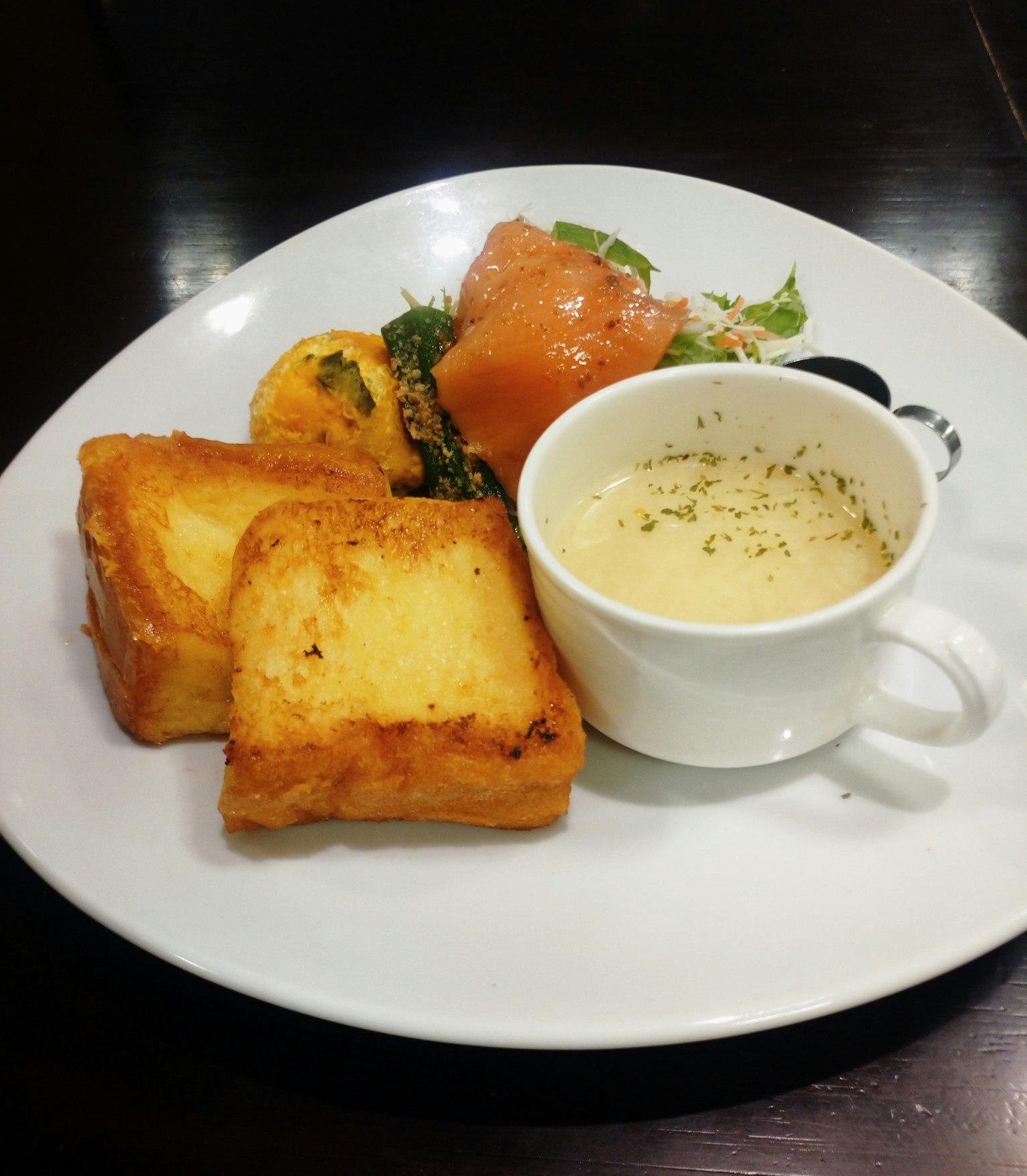 Un piatto con pane tostato, salmone, insalata e zuppa di crema