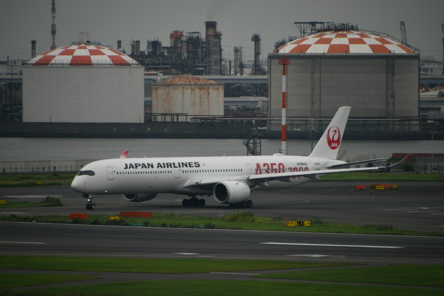 Máy bay Japan Airlines đang di chuyển trên đường băng với các bể chứa đỏ và trắng ở phía sau