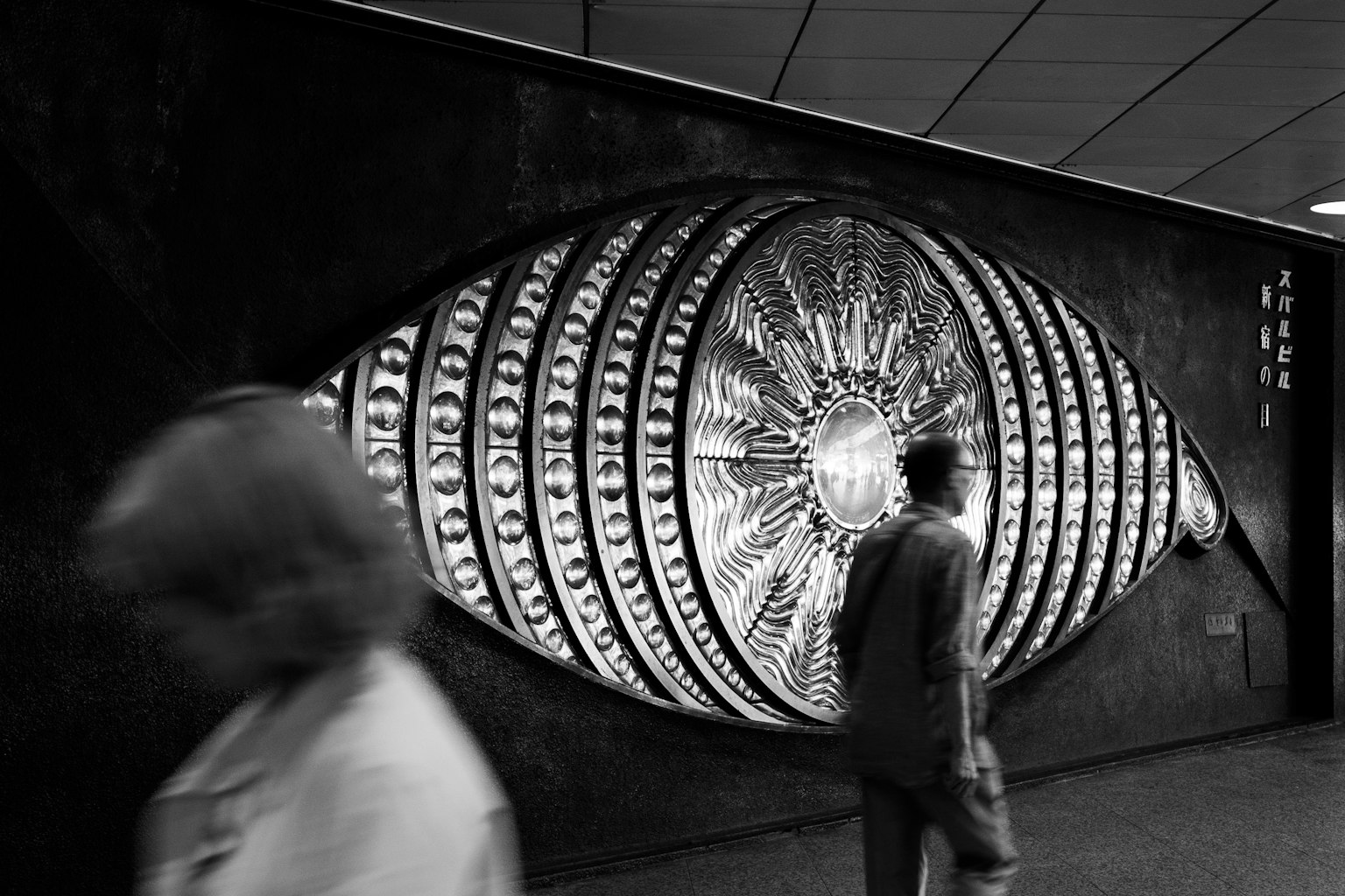Large eye art installation on a black wall with pedestrians walking by