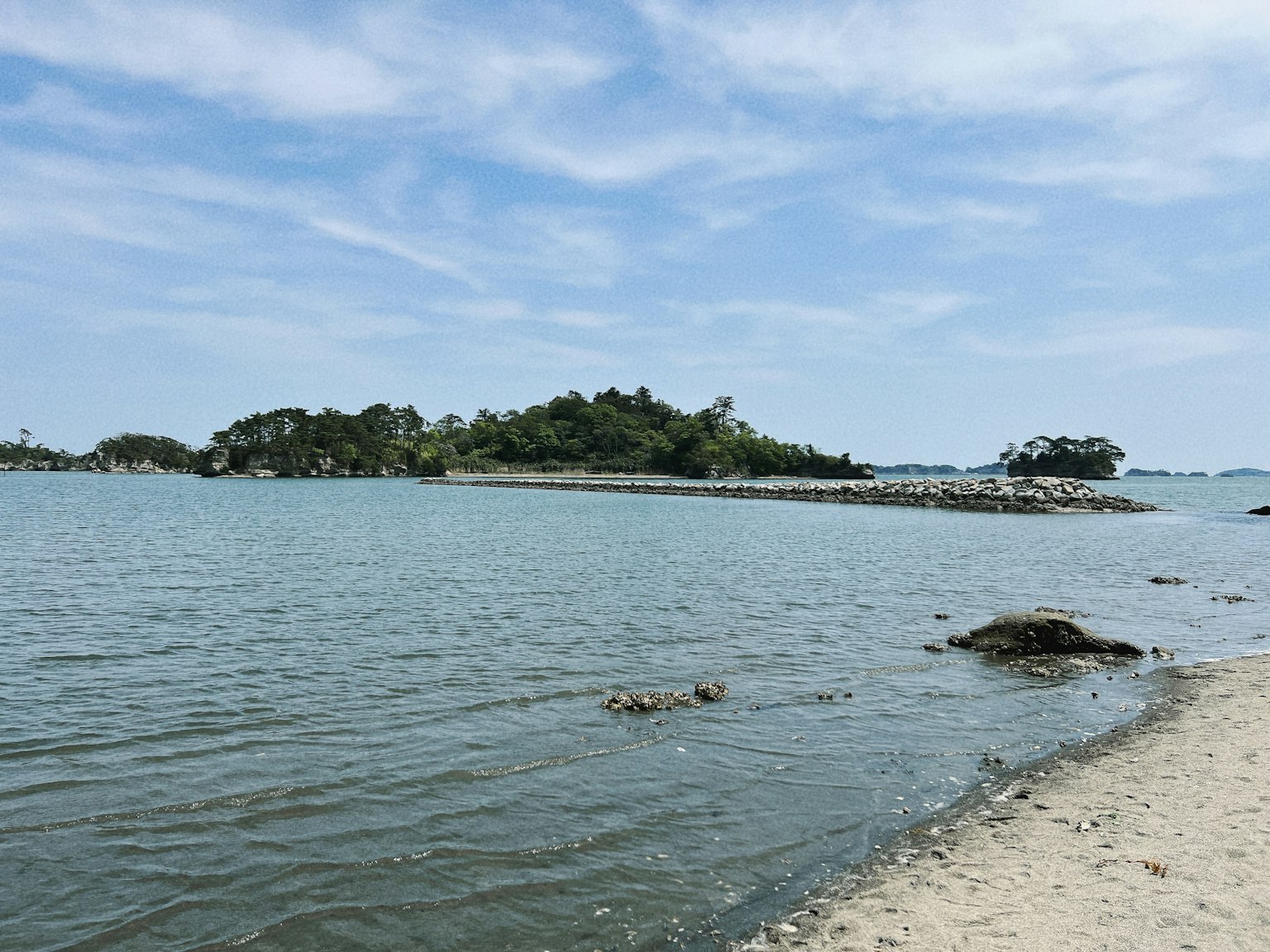 Serene beach landscape featuring calm waters a small island and a blue sky