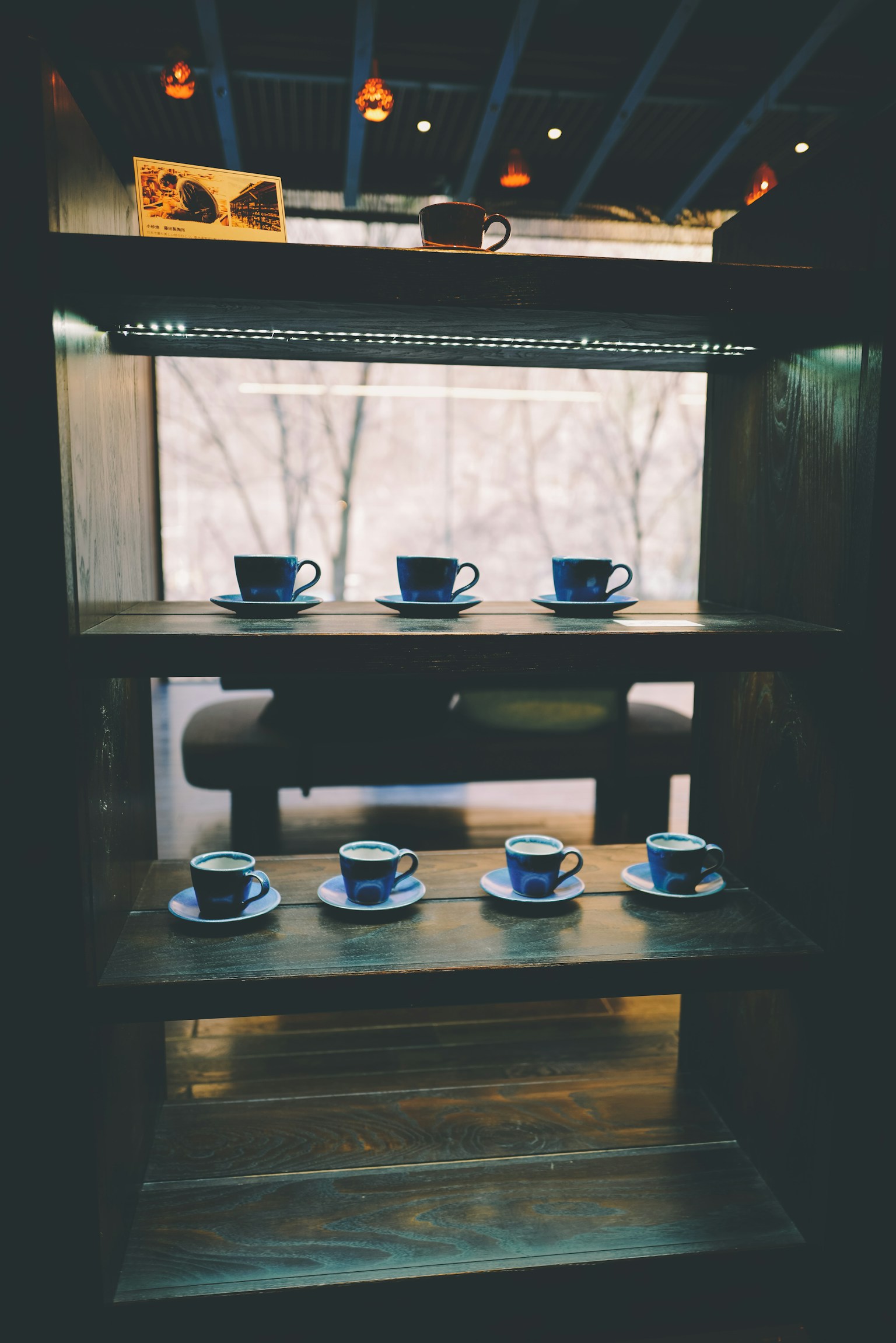 木製の棚に並んだ青いカップと皿のセットがあるコーヒーショップの内部