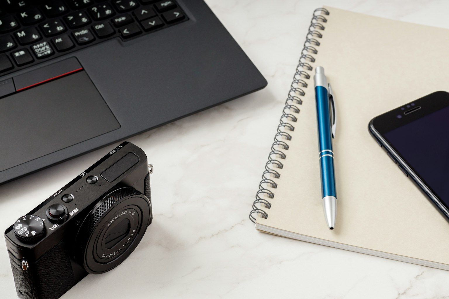 Una scena da scrivania con una fotocamera, un quaderno, una penna e uno smartphone