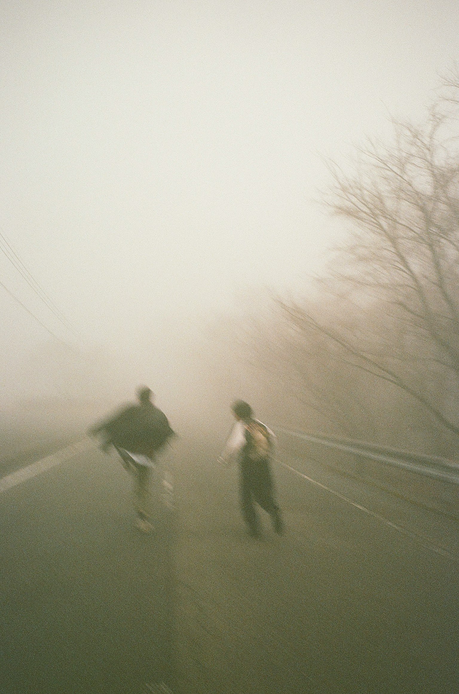 Deux silhouettes courant dans le brouillard sur une route avec des arbres