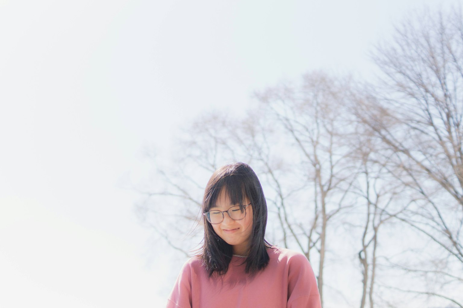 Una donna in maglione rosa chiaro in piedi con alberi spogli sullo sfondo