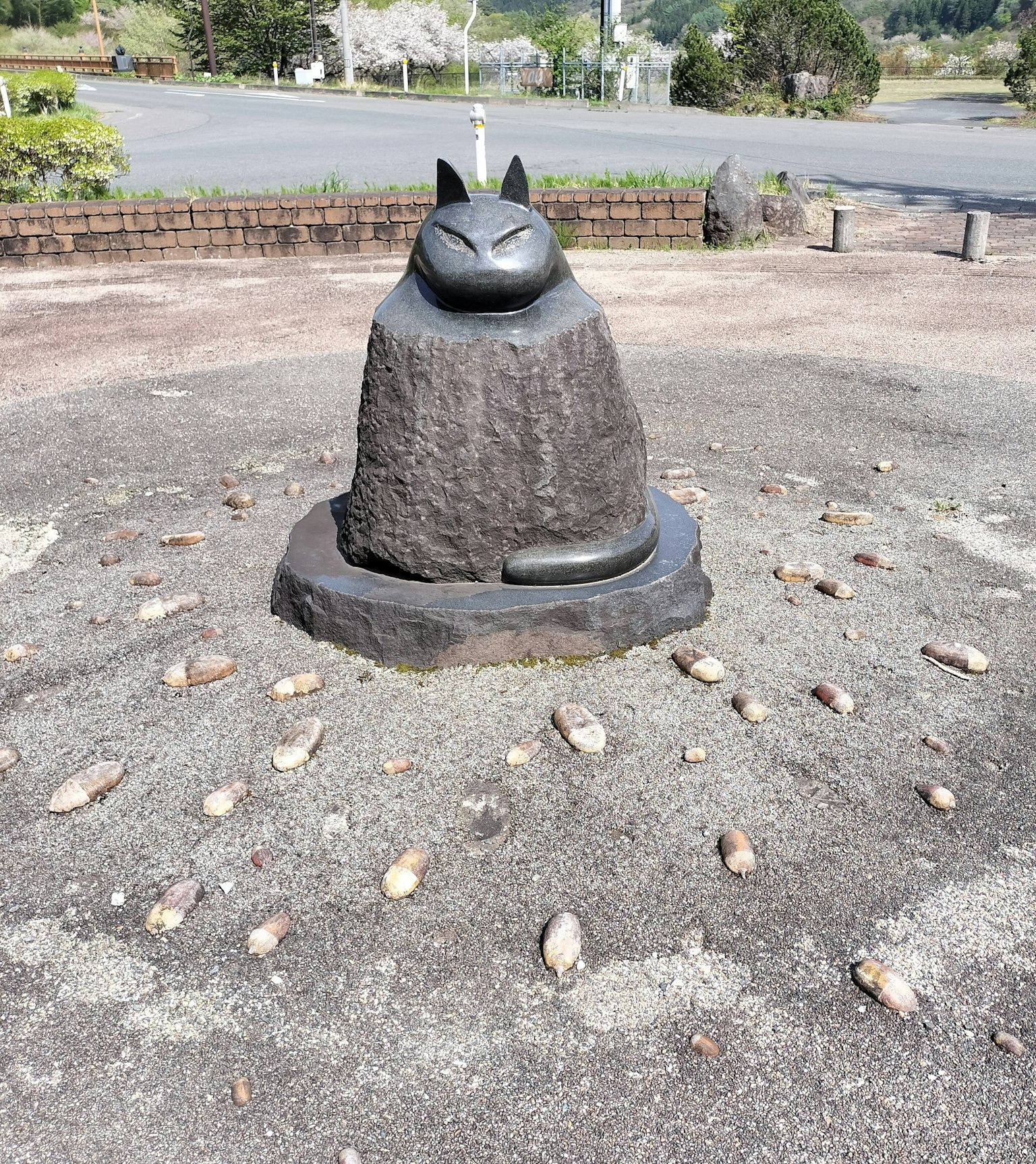 Scultura di un gatto nero su un piedistallo di pietra circondata da ciottoli