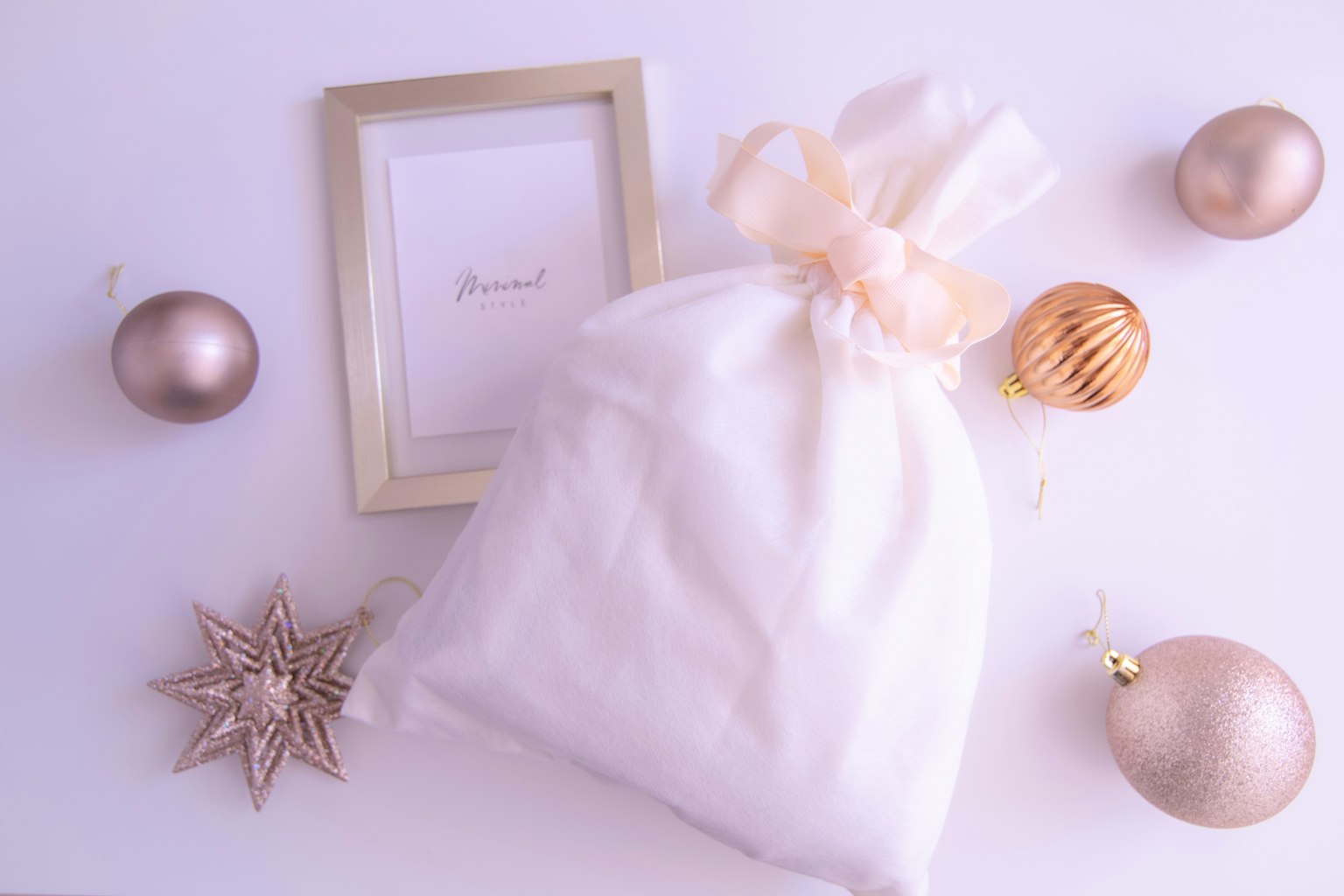 White gift bag with a ribbon surrounded by golden ornaments and a picture frame