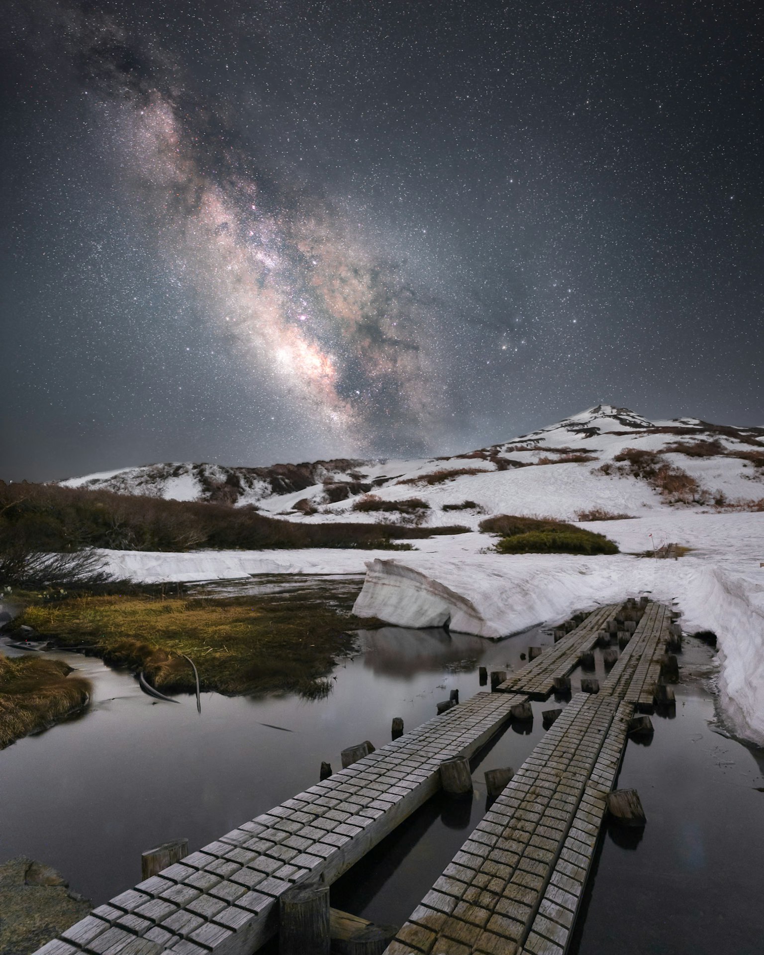 Galassia sopra una montagna innevata con un ponte di legno che si riflette nell'acqua