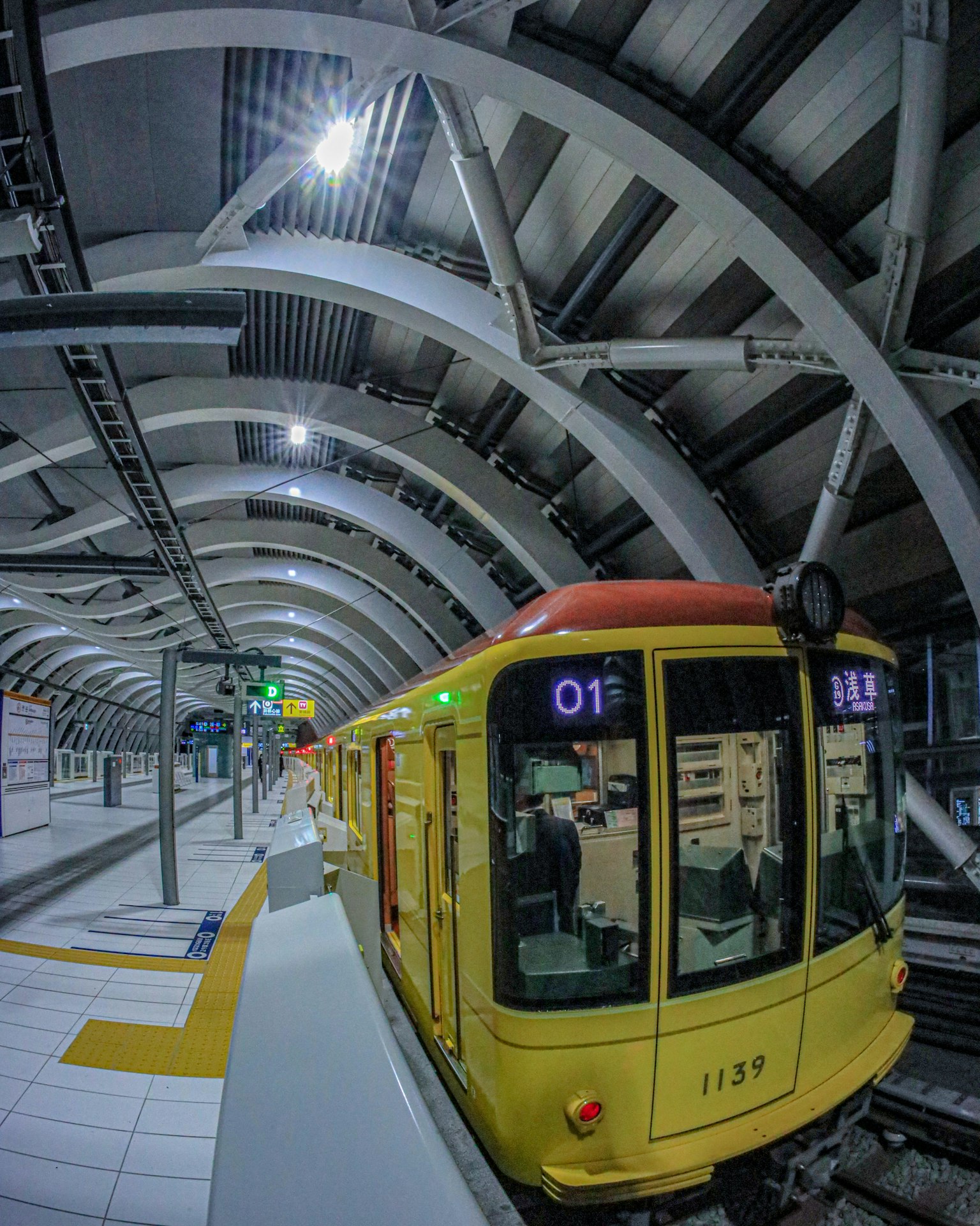 Kereta kuning di stasiun modern dengan arsitektur melengkung dan penandaan platform