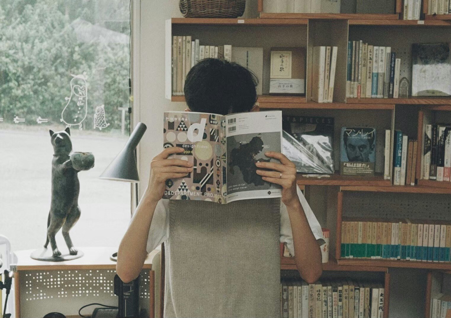 hands holding an open magazine in front of a bookshelf