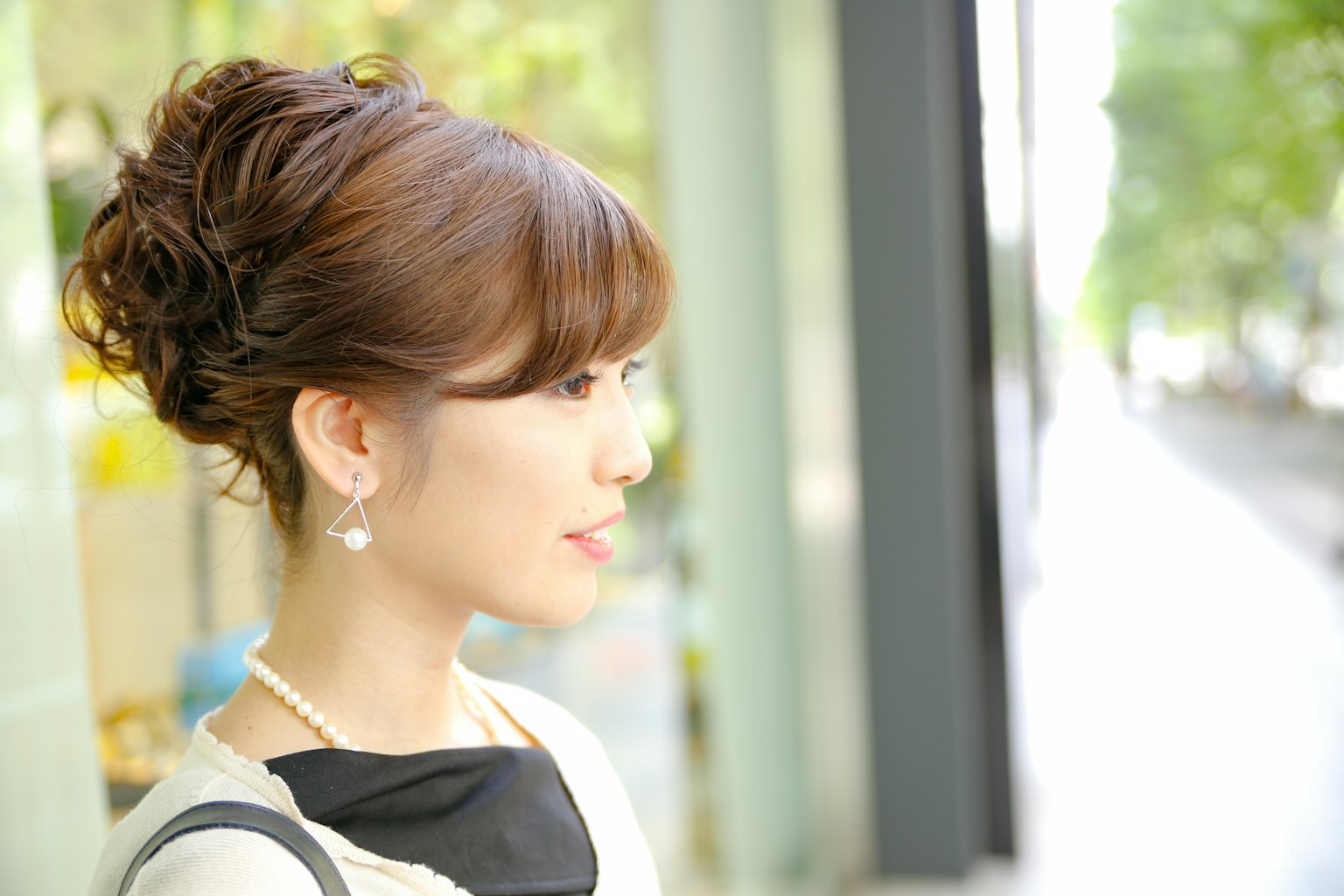Profil wanita dengan gaya rambut diikat mengenakan anting-anting mutiara dengan latar belakang perkotaan