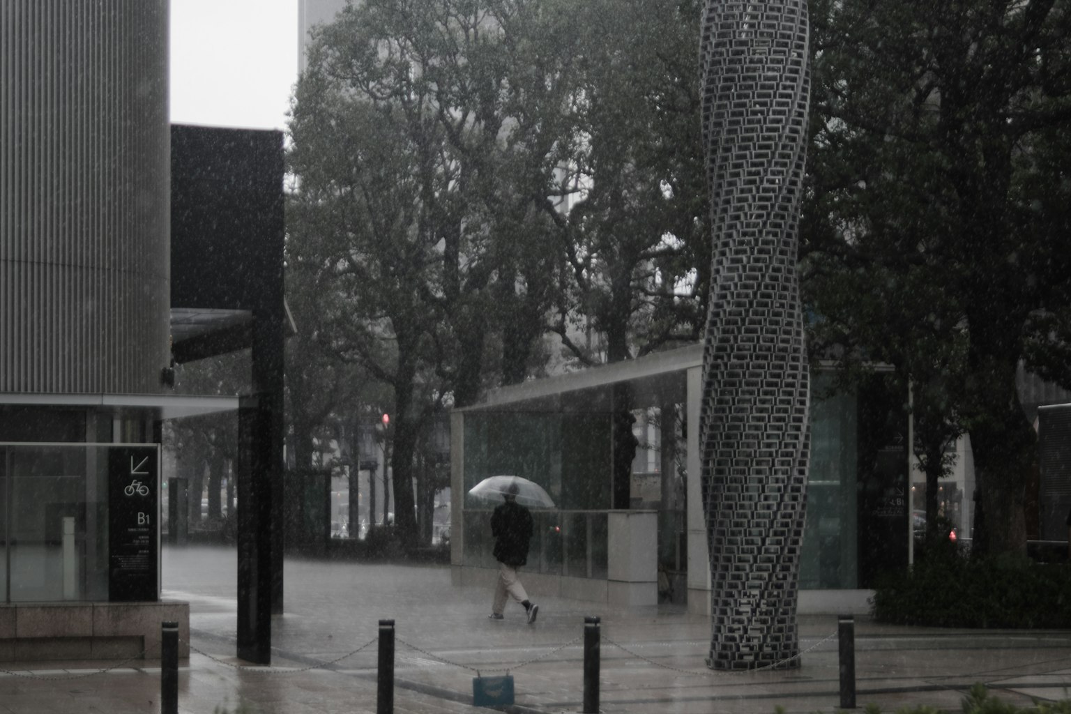 Persona che cammina con un ombrello sotto la pioggia circondata da architettura moderna