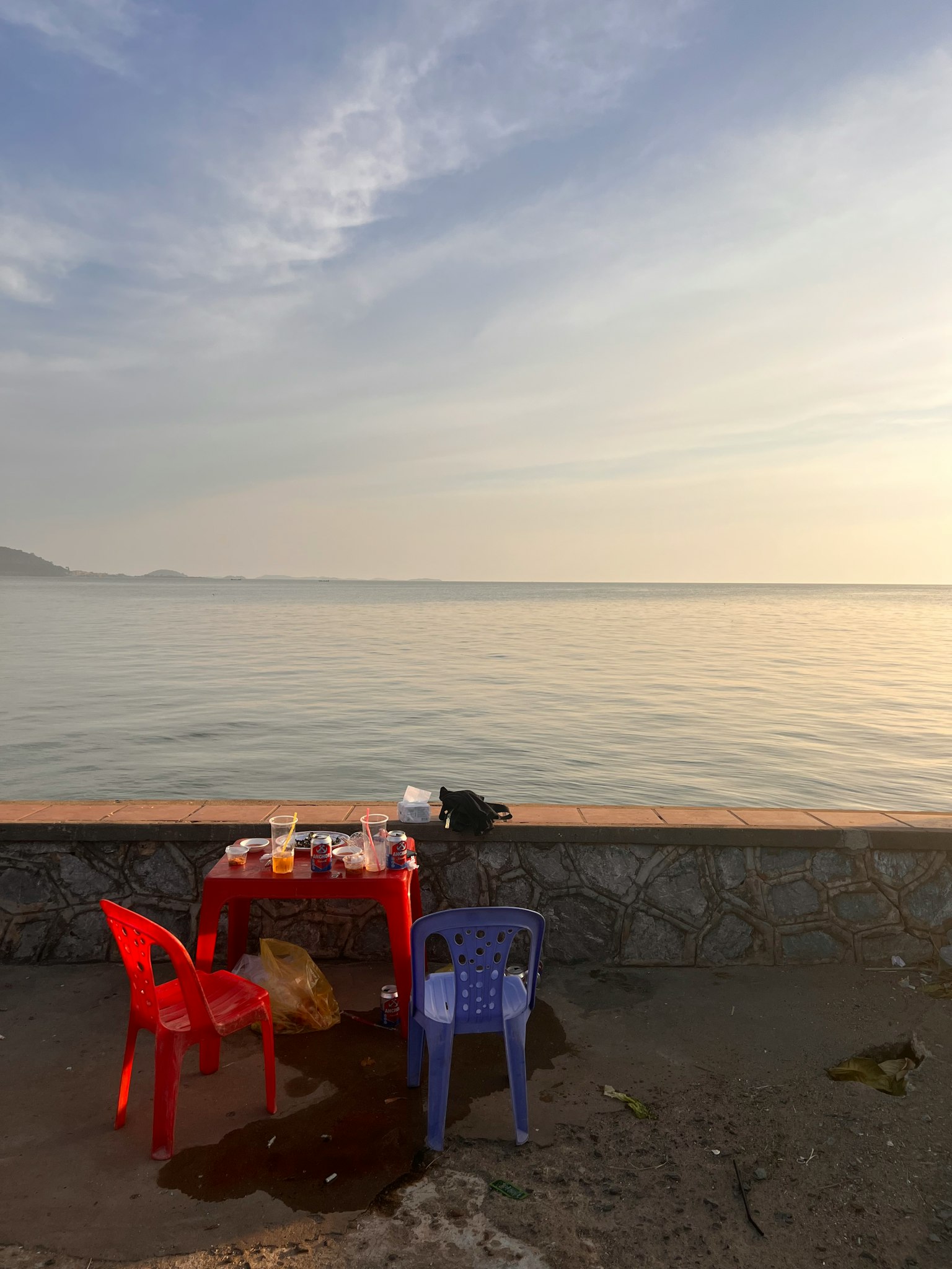 Un set di sedie rosse e blu con un tavolo vicino al mare al tramonto