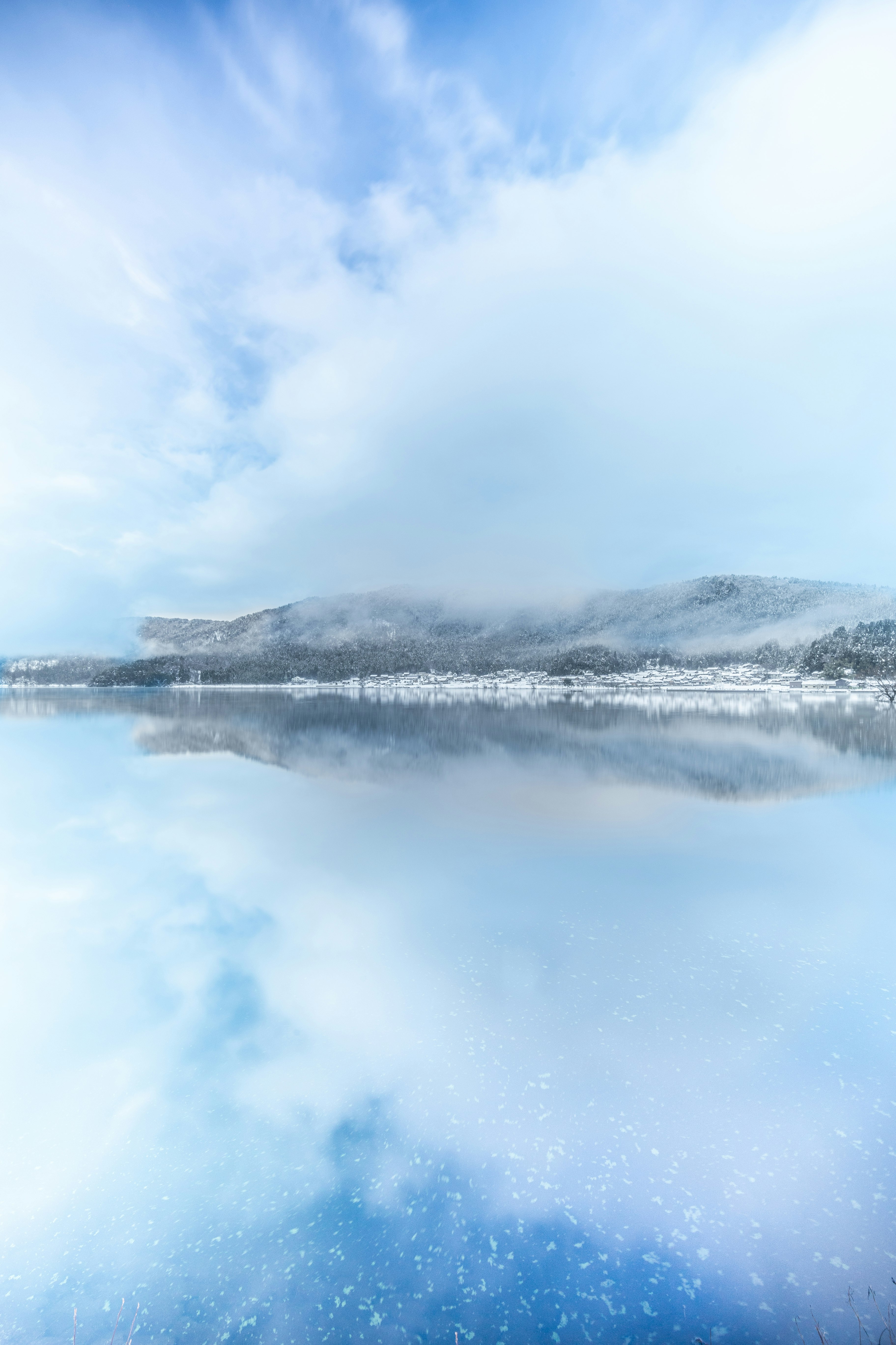 霧に包まれた湖畔と雪の山並みの静かな風景