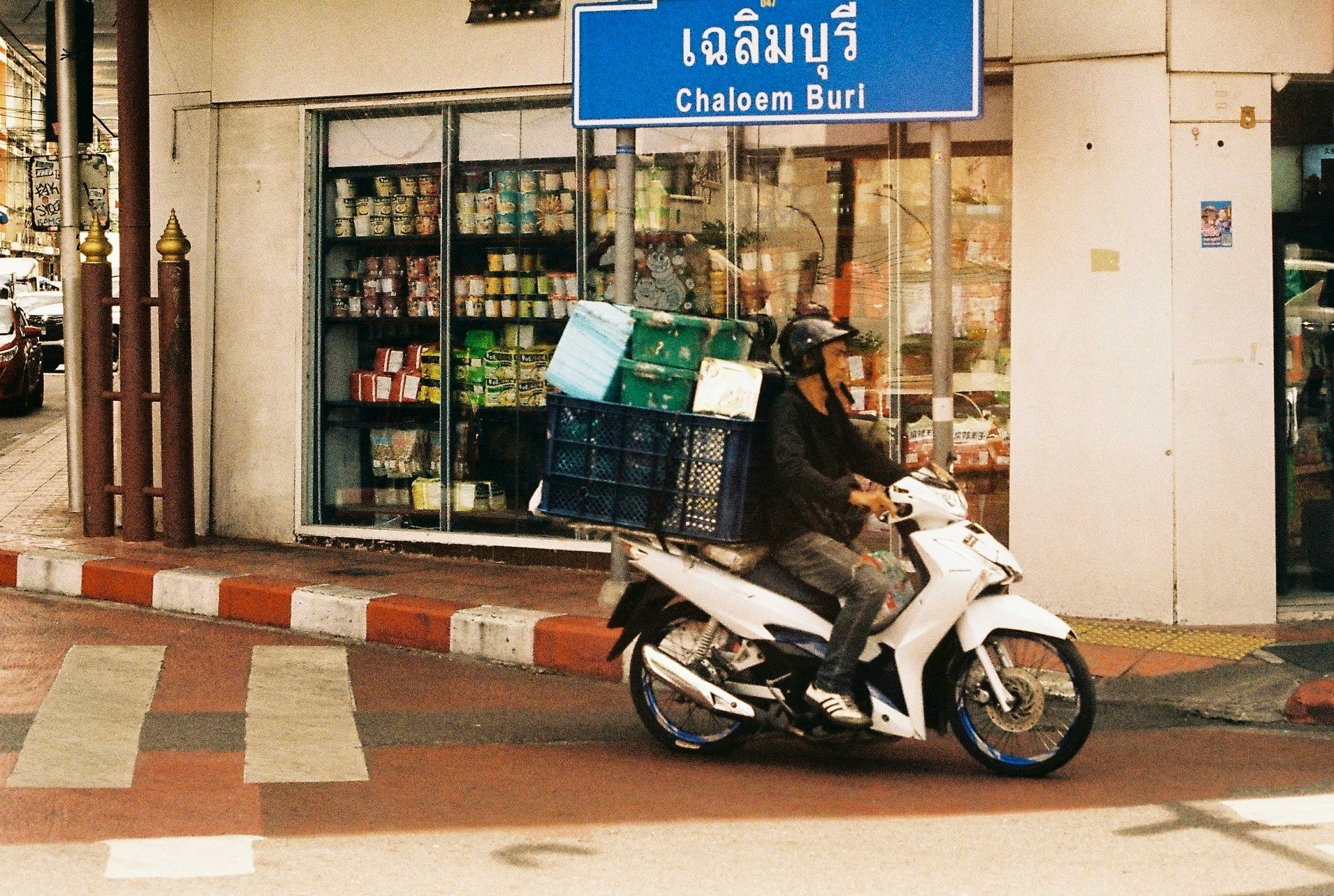 青い看板「Chaloem Buri」のある路地のバイクと店先
