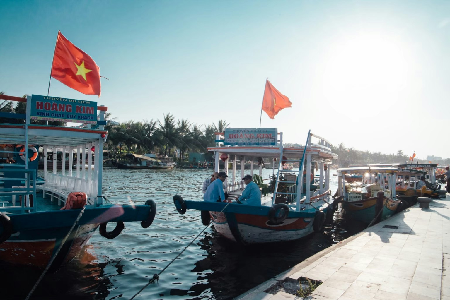 เรือสีสันสดใสจอดอยู่ที่แม่น้ำในเวียดนามพร้อมธงแดง