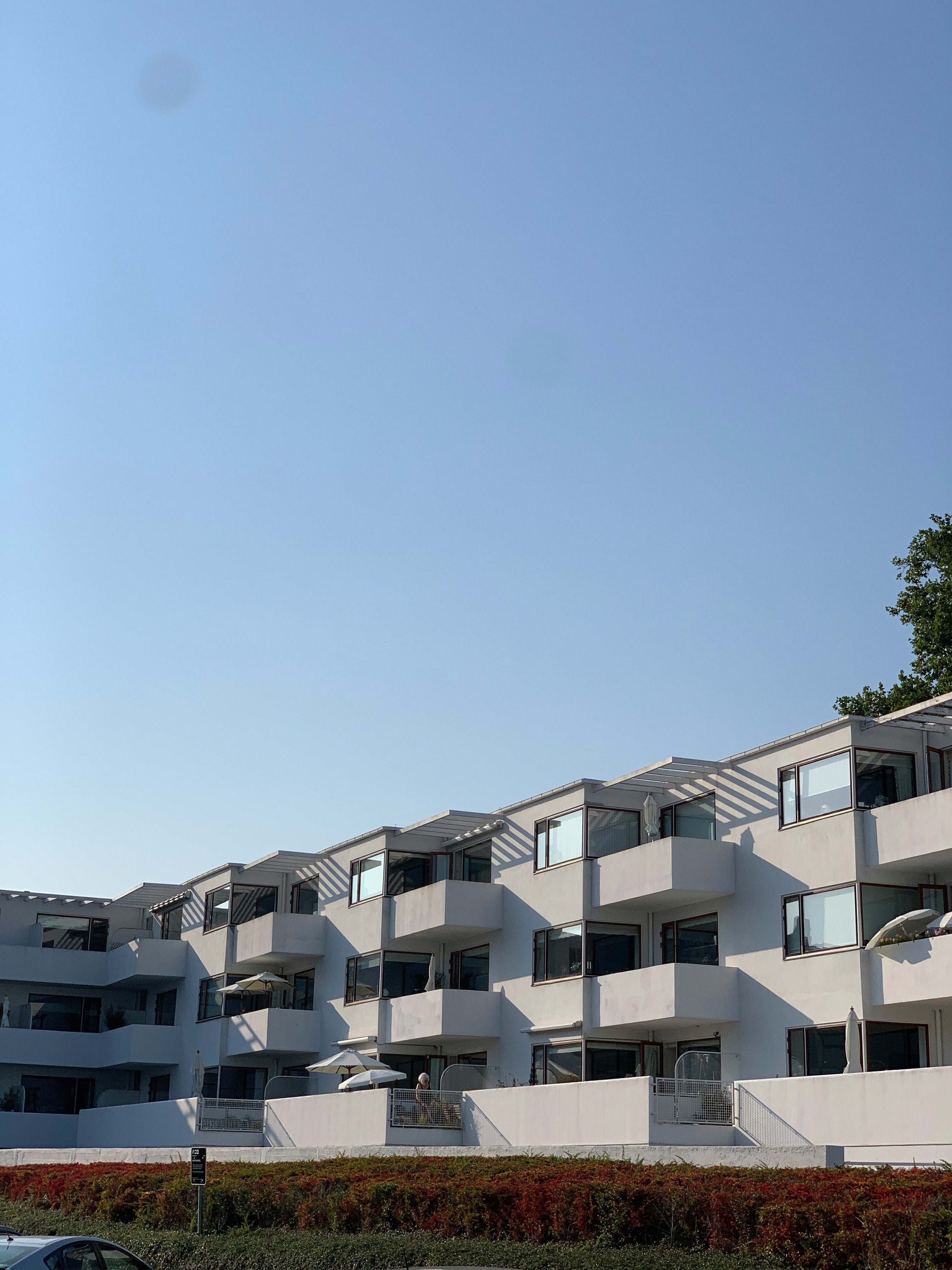 青空の下に並ぶ白いテラス付き集合住宅の外観