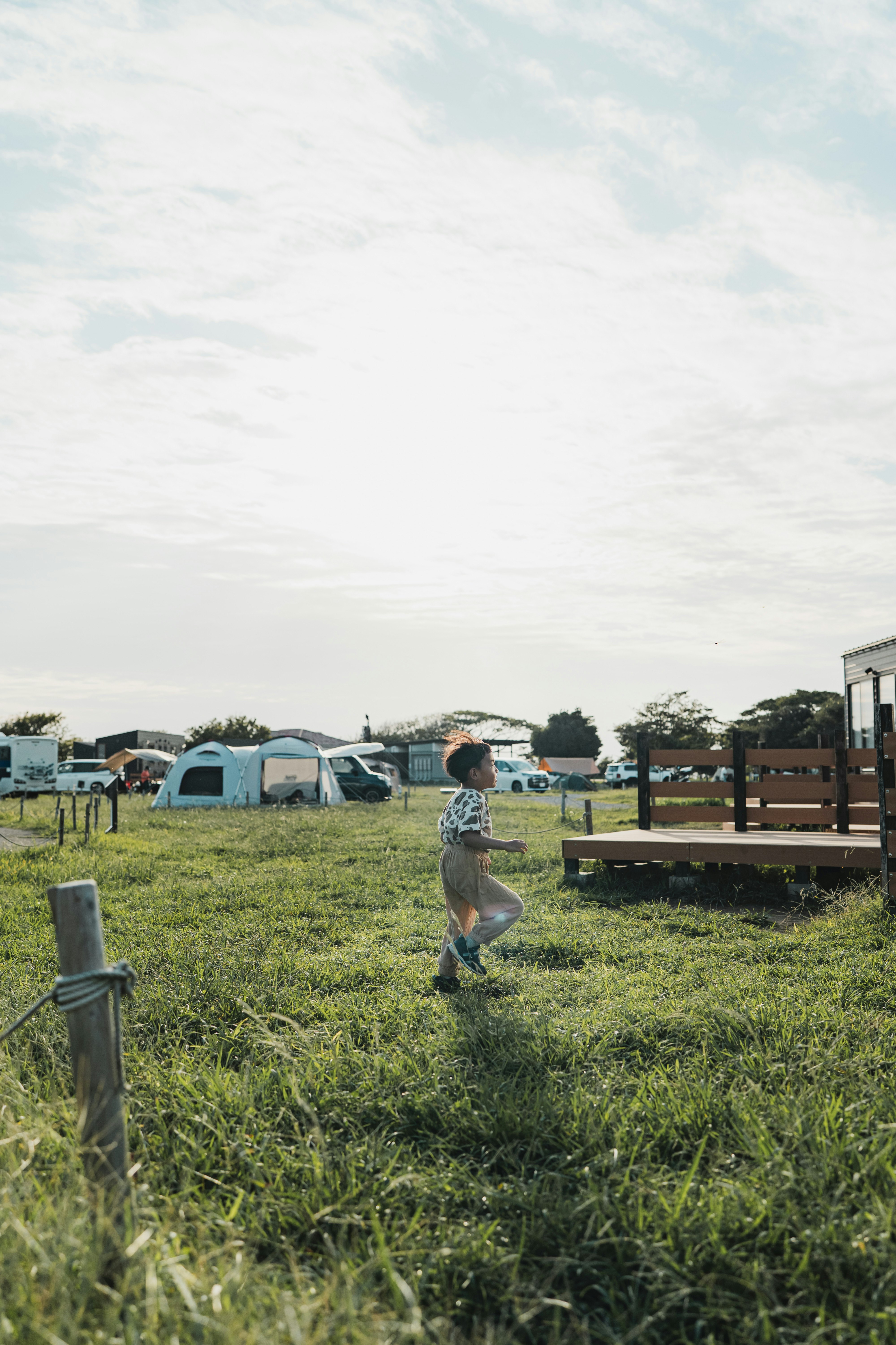 Un enfant courant dans un camping herbeux avec des remorques et une terrasse en bois