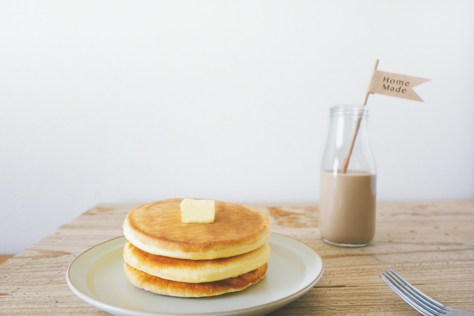 Tre pancake impilati con una noce di burro sopra e una piccola bandiera in una bottiglia di vetro