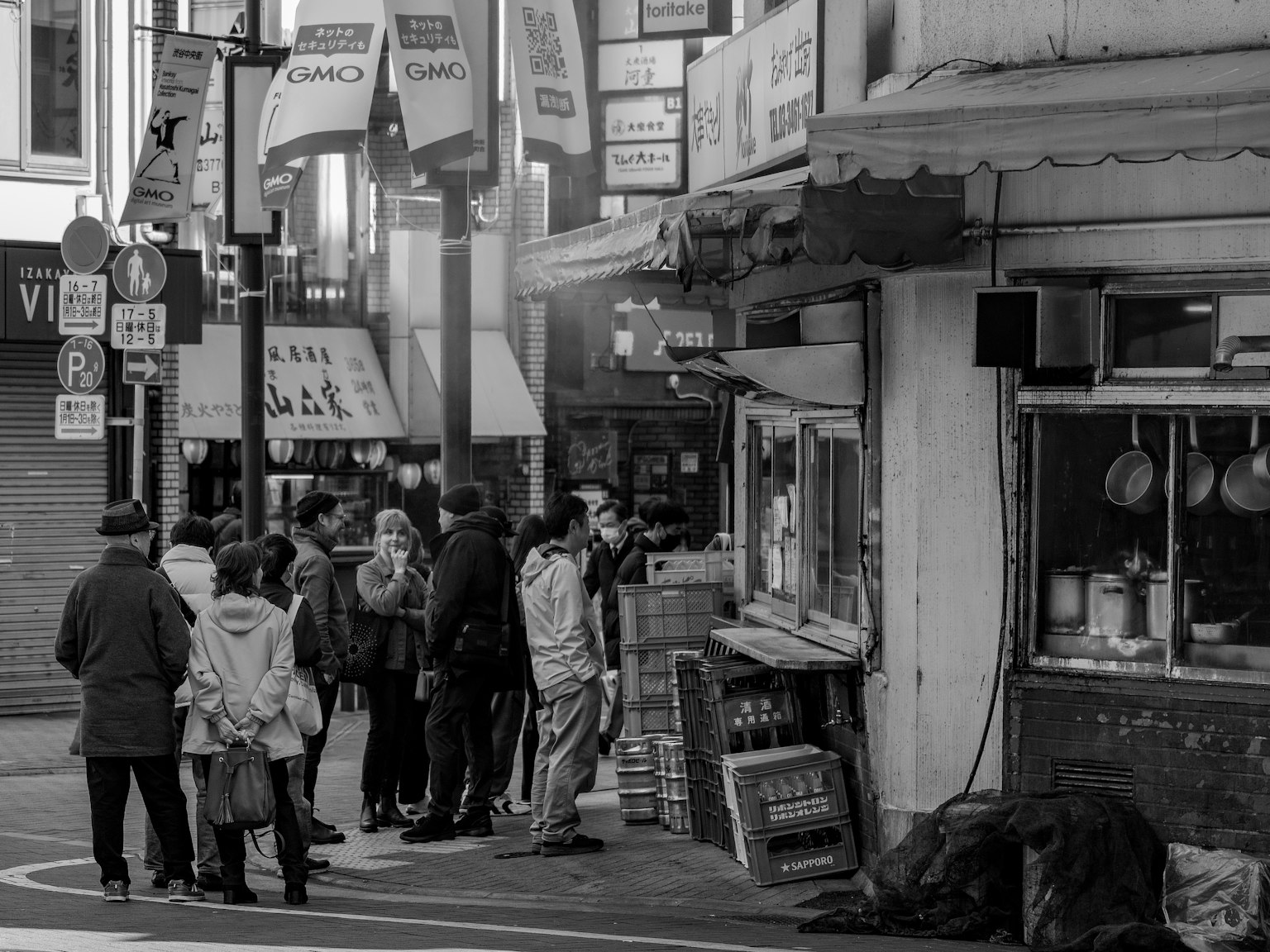 ภาพถนนขาวดำที่มีผู้คนยืนเรียงแถวหน้าร้านอาหาร