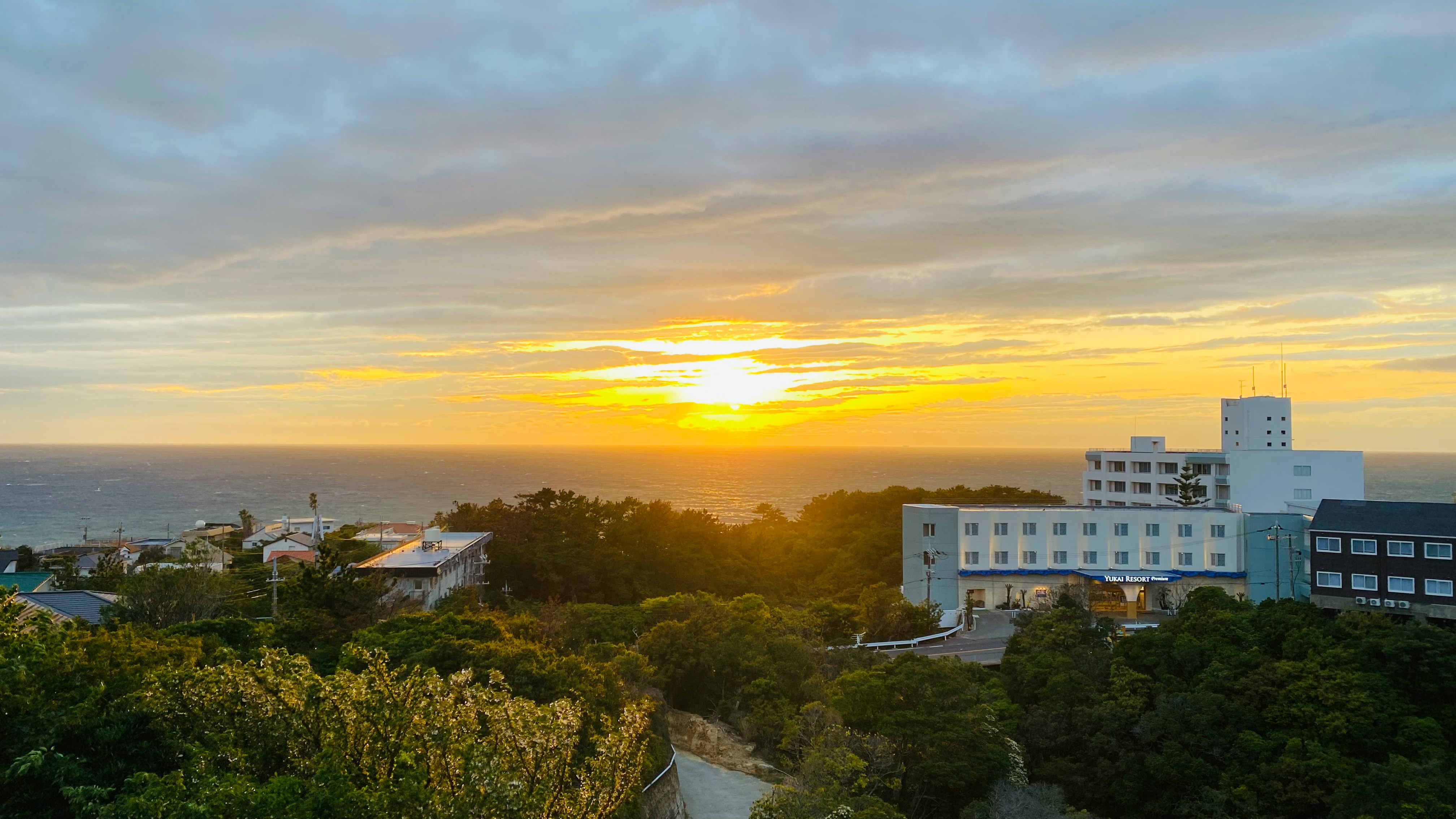 夕焼けの海辺と森の上に建つ白い建物群